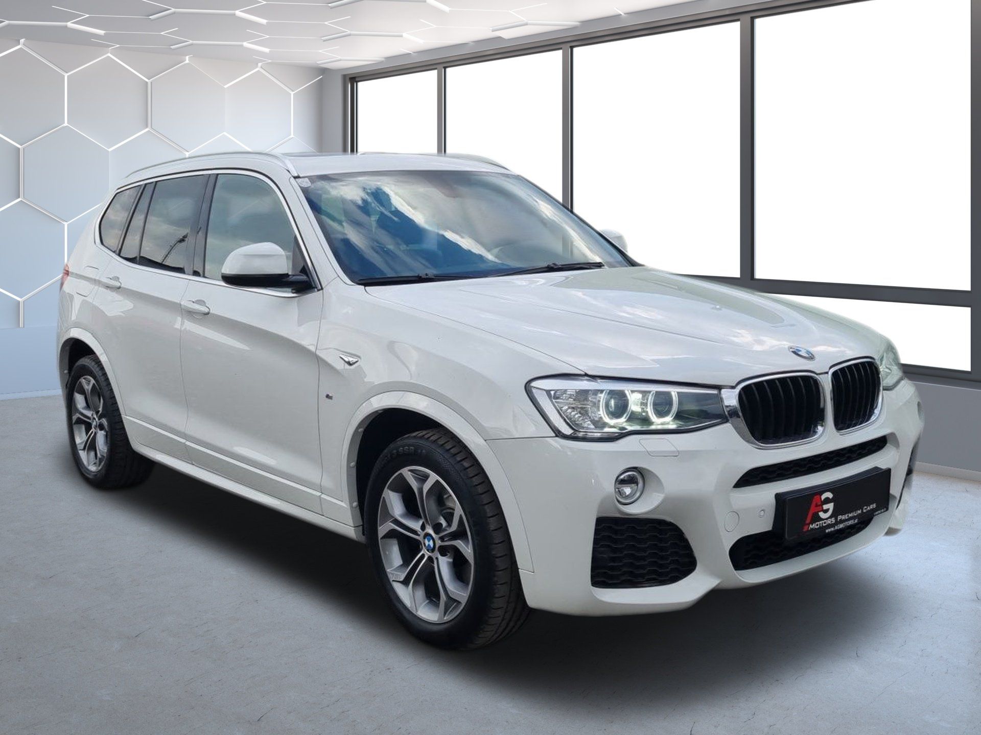 Biele SUV BMW v presvetlenej predajni, pohľad zľava spredu, zaparkované na naleštenej podlahe.