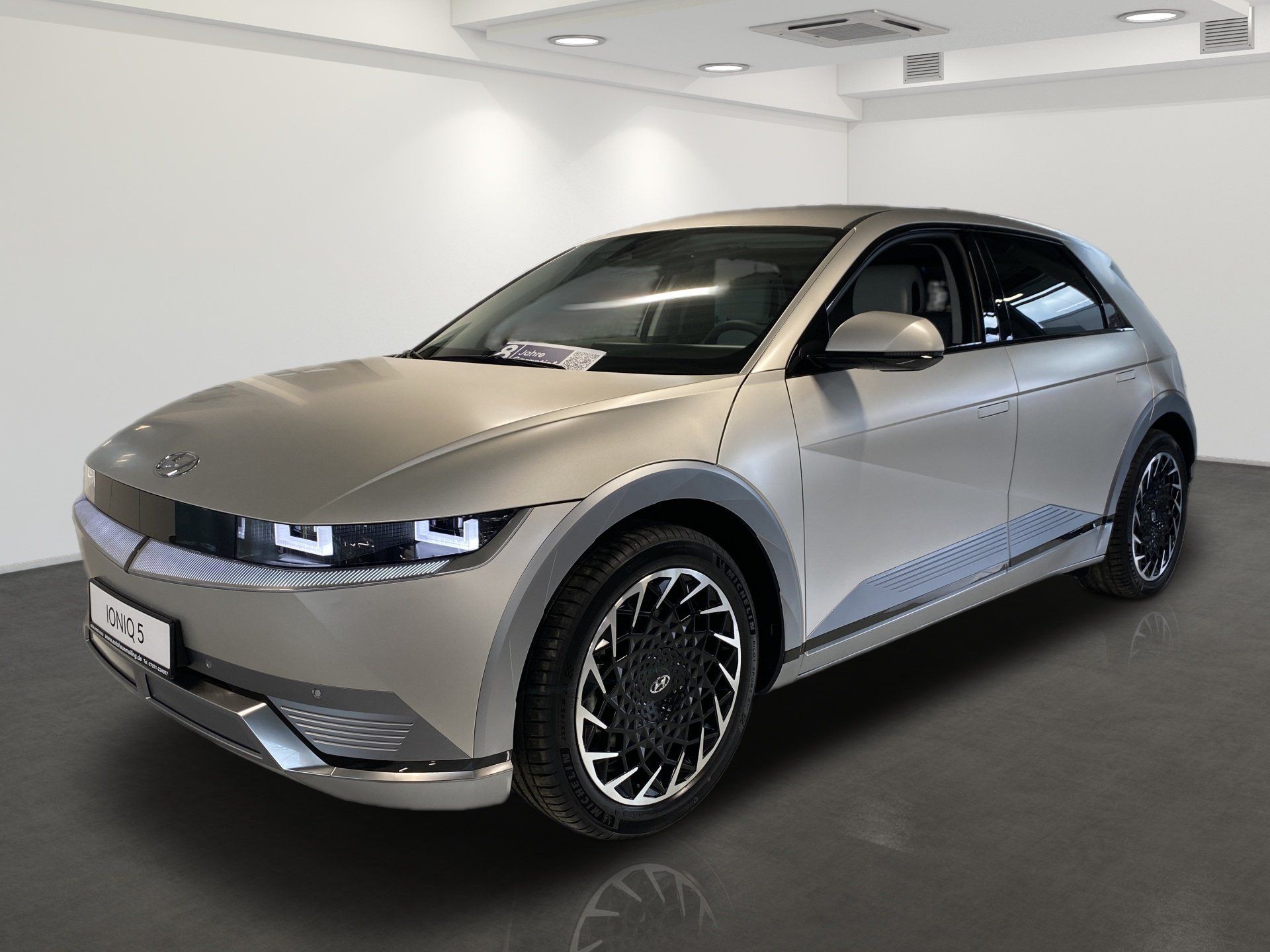 Silver hatchback electric car in a white showroom, front-left view