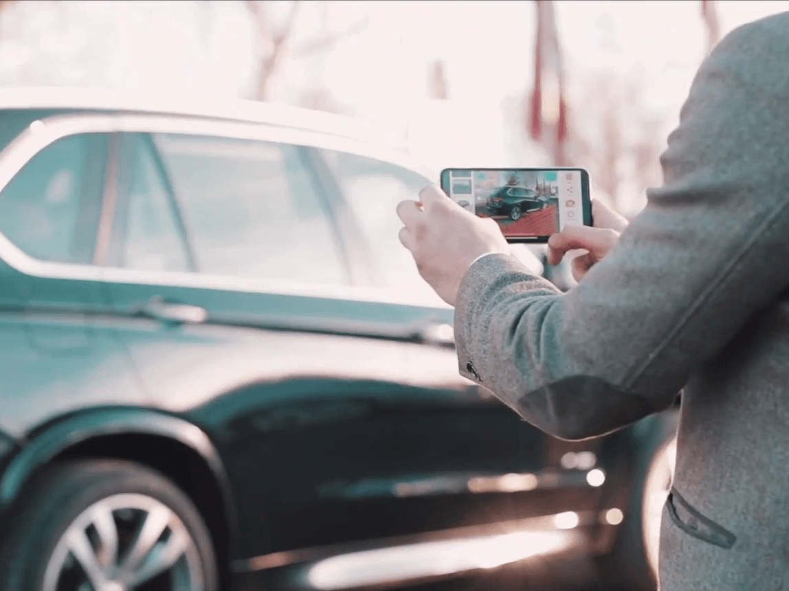 Person photographing a black car with a smartphone outdoors