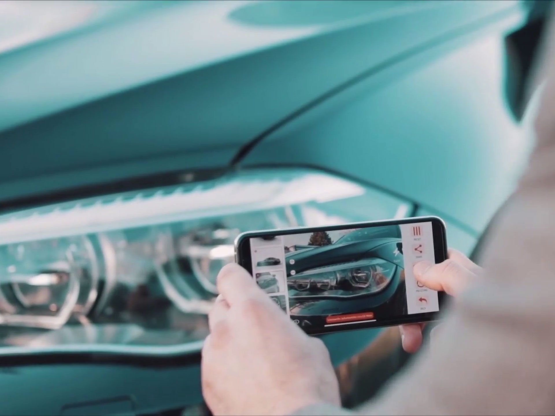 Hands photographing a teal car’s front headlight and grille with a smartphone