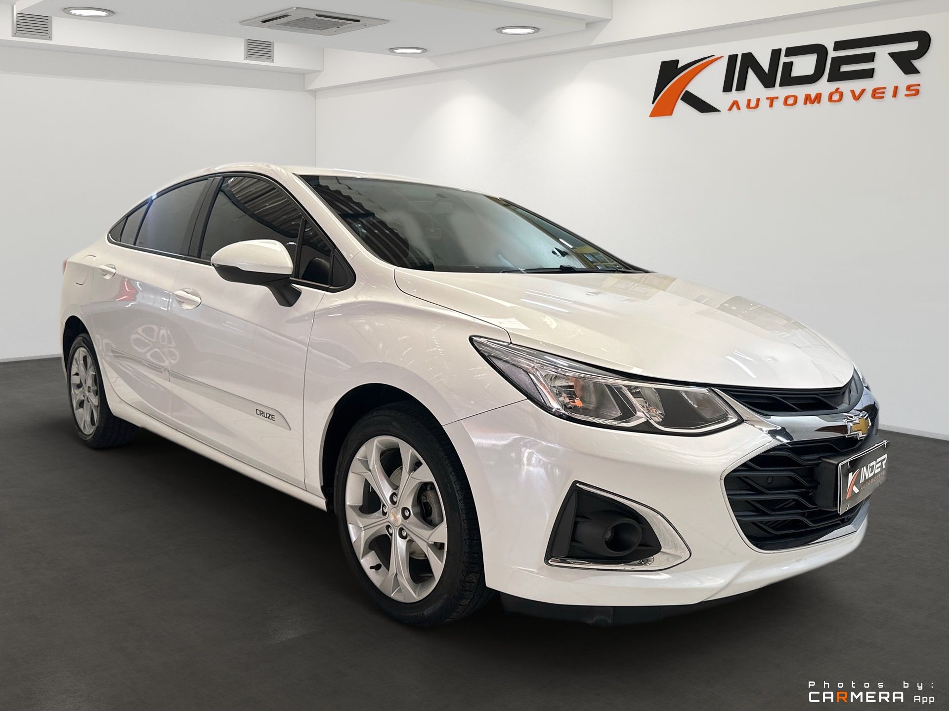 Biely sedan v showroome s logom Kinder Automóveis na stene