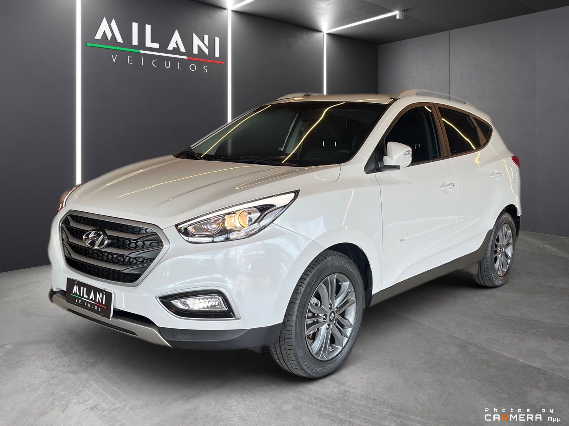 Biele SUV vystavené v showroome s tmavými stenami a nápisom MILANI