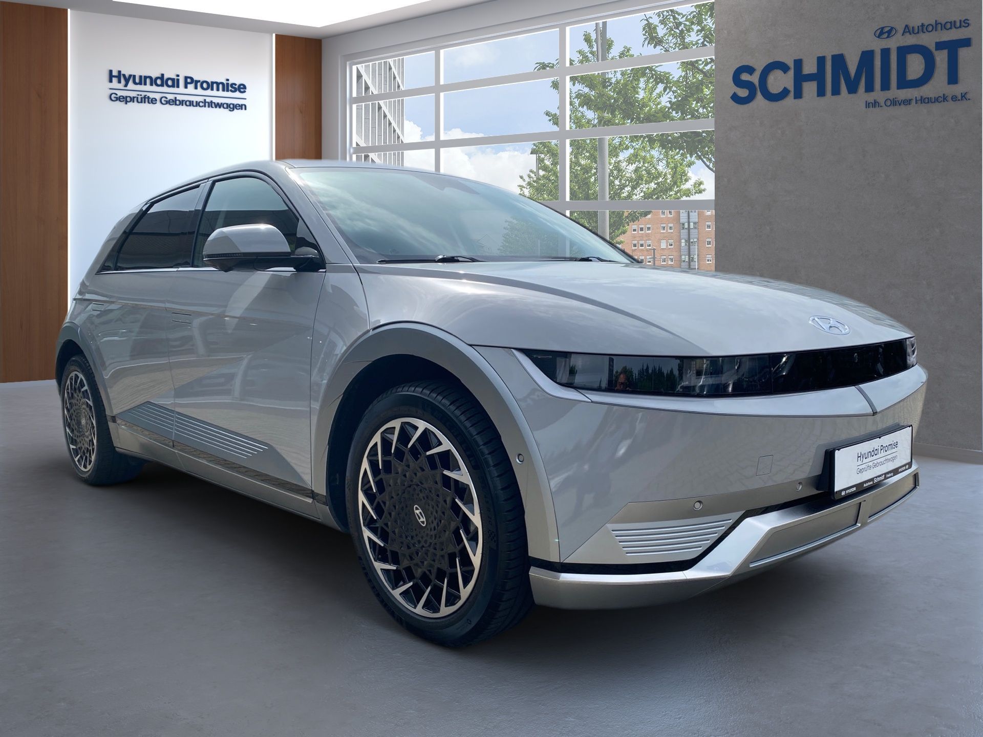 Strieborný elektrický hatchback v showroome s logom Schmidt a veľkými oknami.