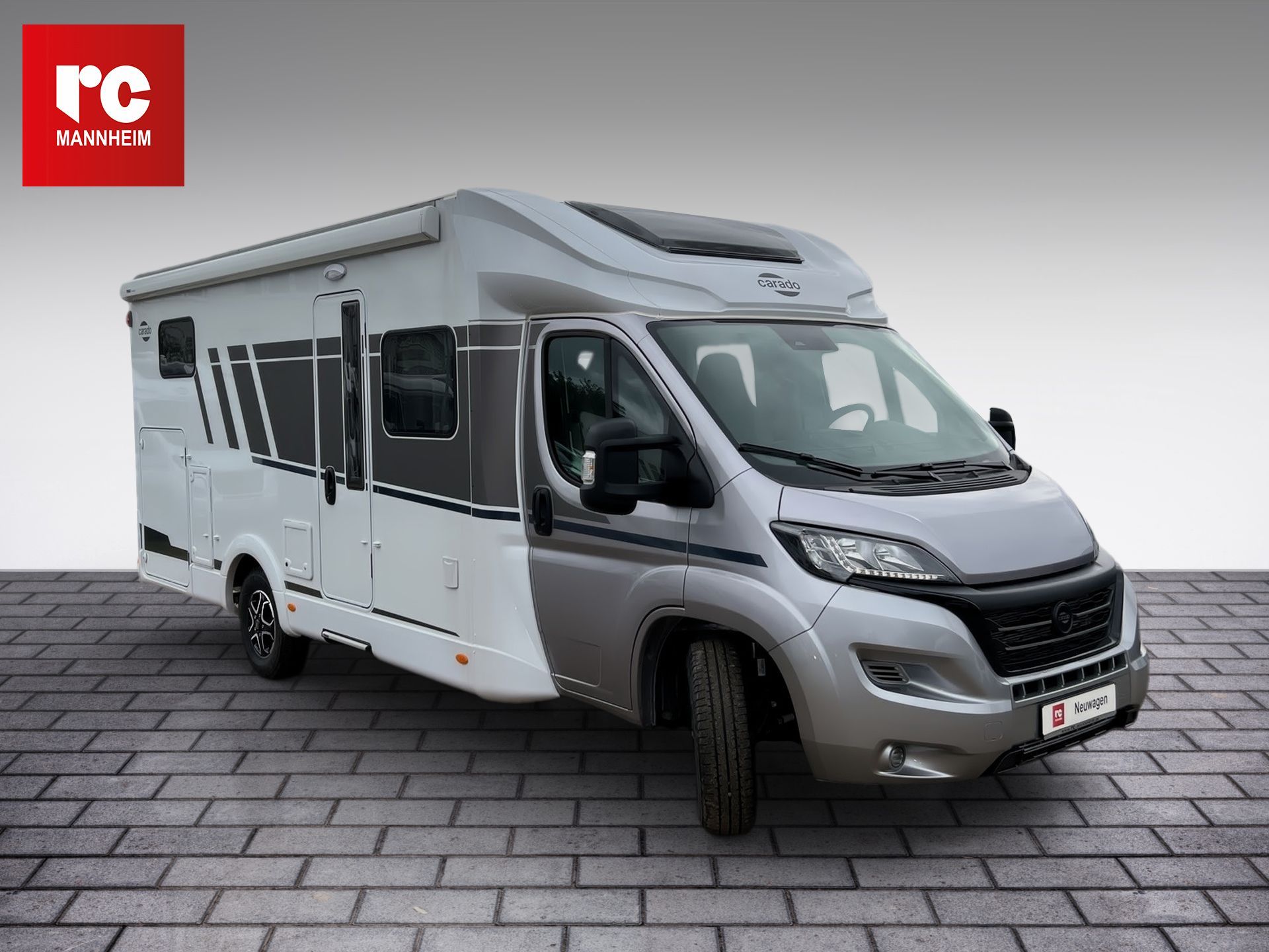 Strieborný obytný automobil s výsuvnou markízou, zaparkovaný na tehlovom povrchu na sivom pozadí