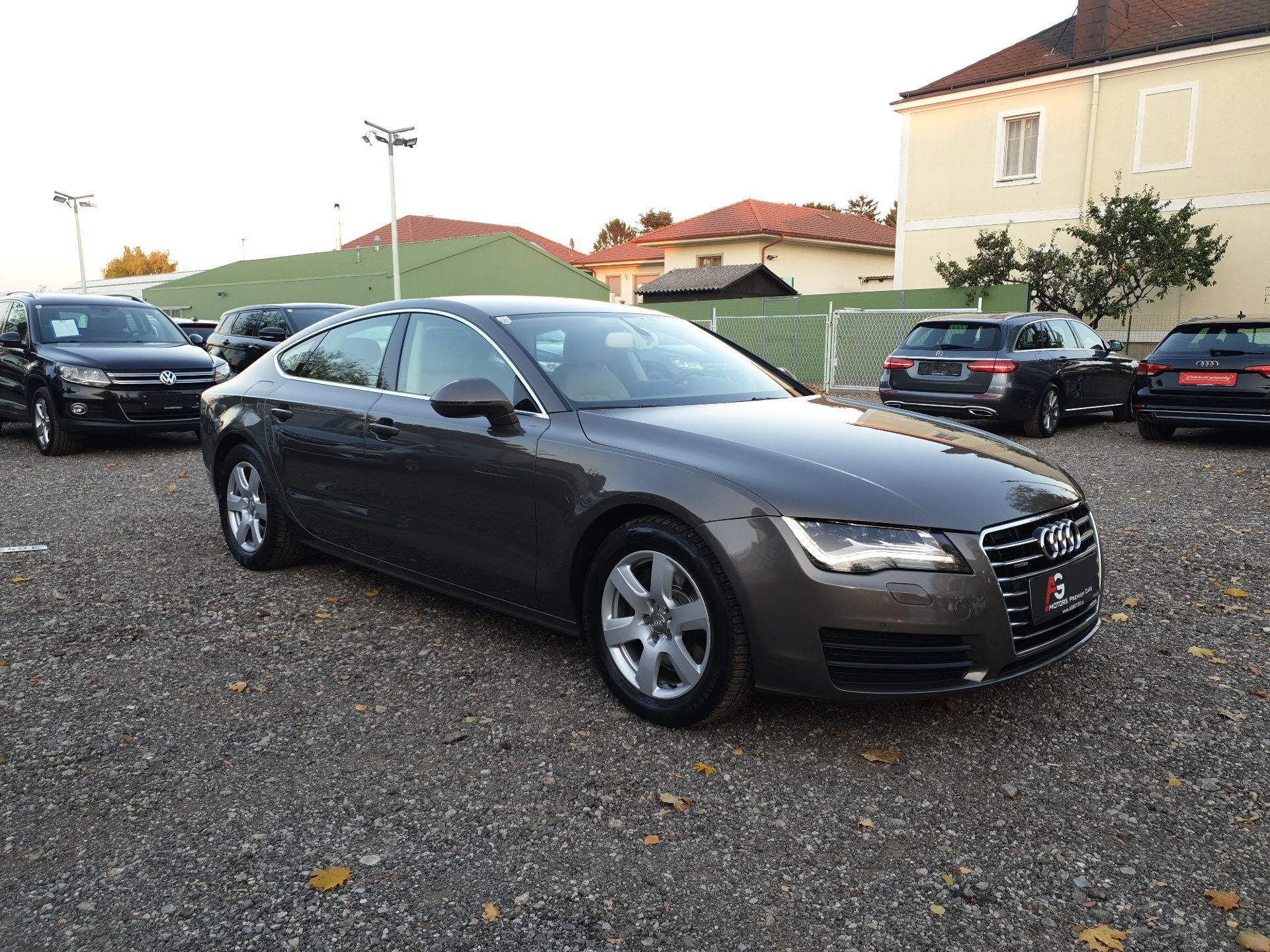 Dark gray Audi sedan parked on a gravel lot near houses and other cars
