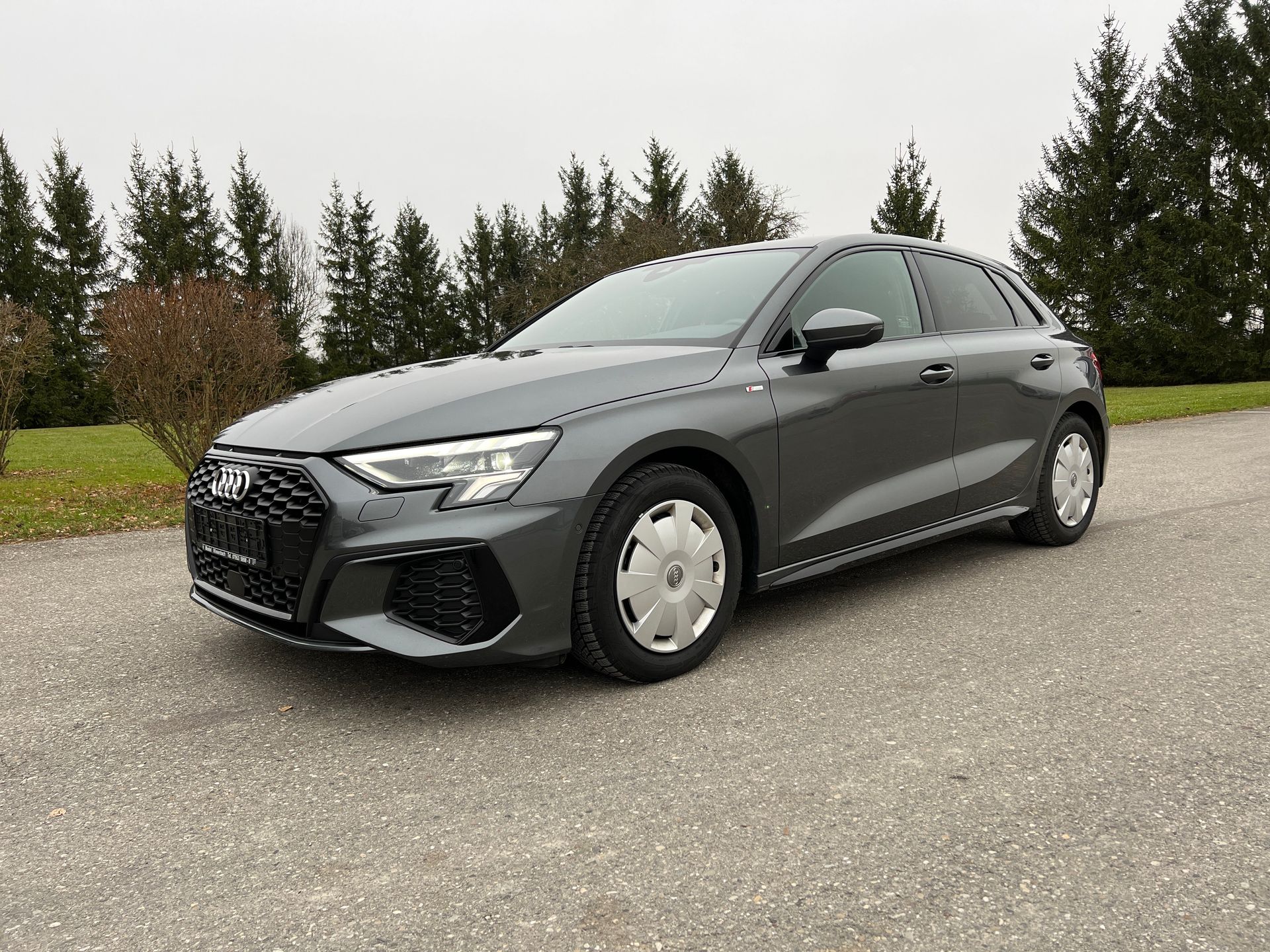 Gray sedan parked on a gravel lot with trees in the background
