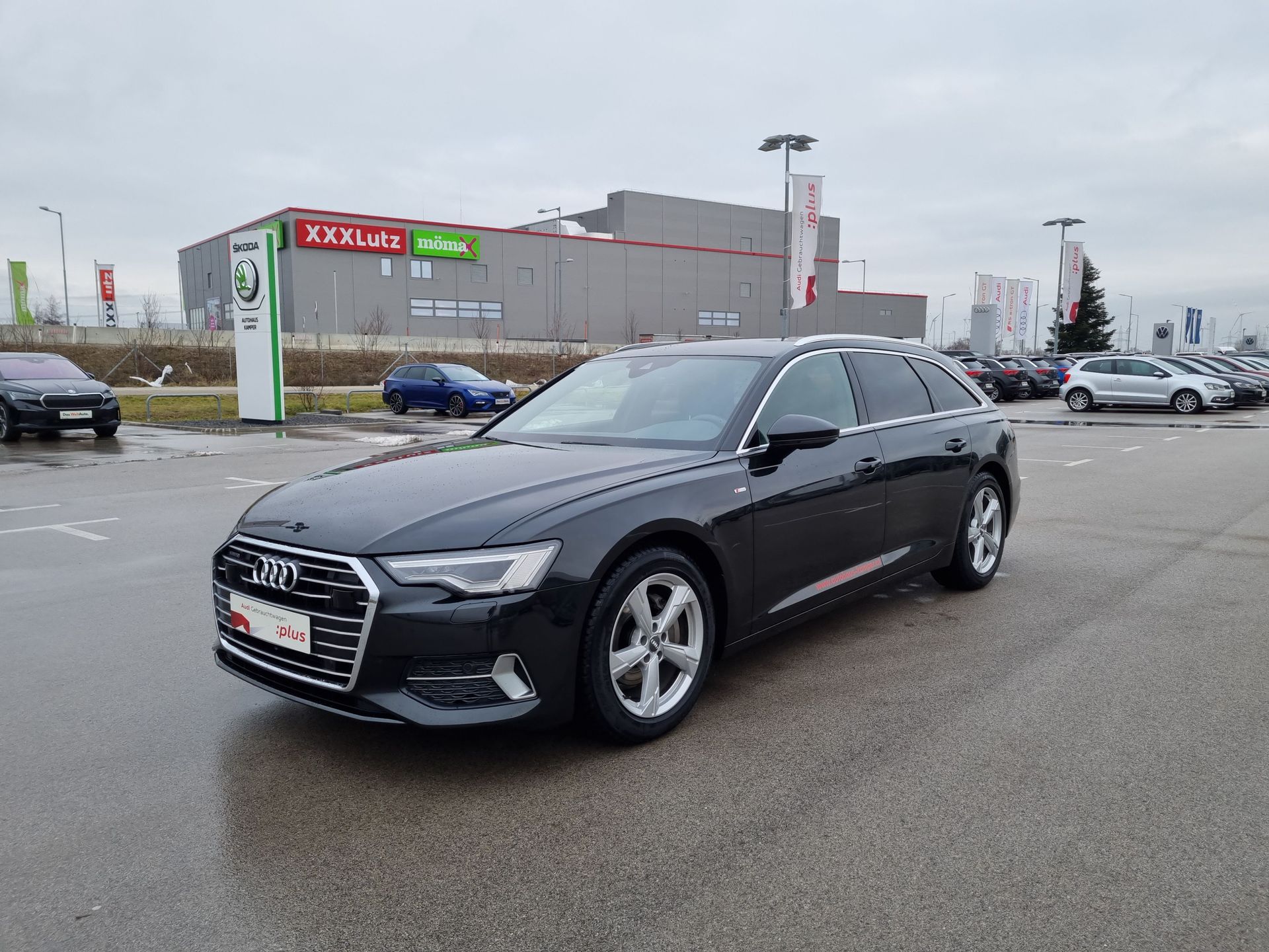 Black Audi sedan parked in a wet dealership lot under an overcast sky
