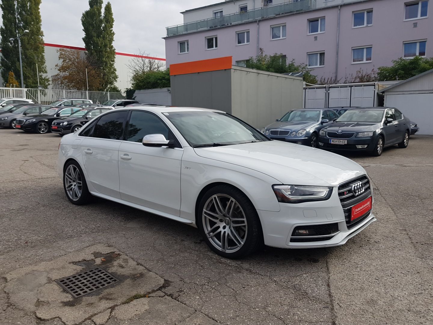 White Audi sedan parked in a lot beside other cars and apartment buildings