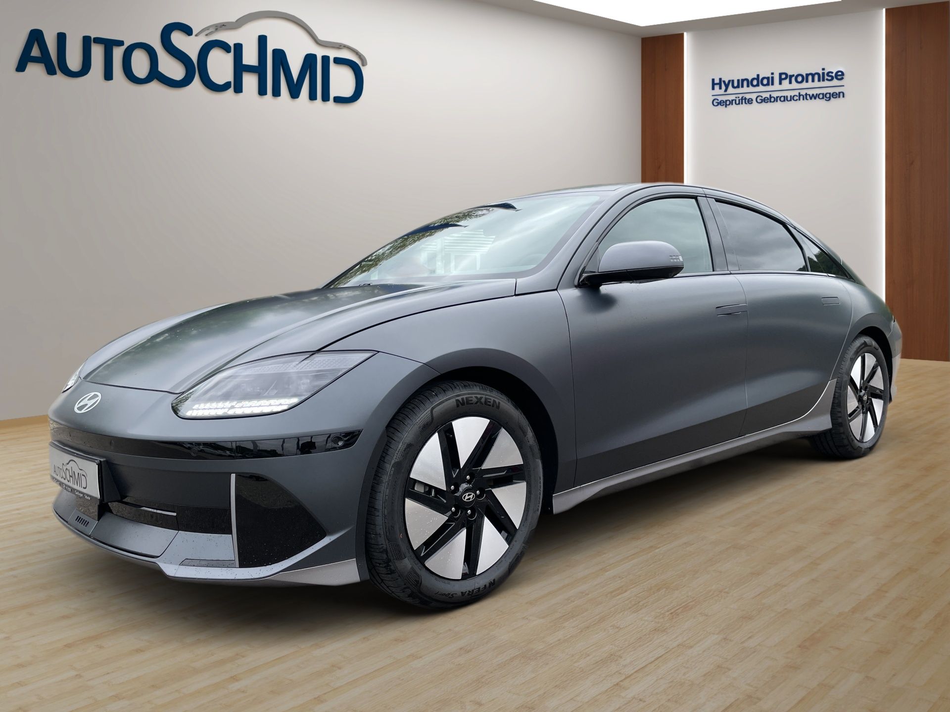 Sivý elegantný elektrický sedan v showroome s logom AutoSchmid na stene