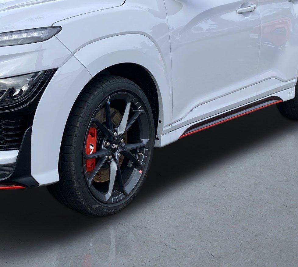 White SUV with black rims and red brake calipers, parked on a gray floor