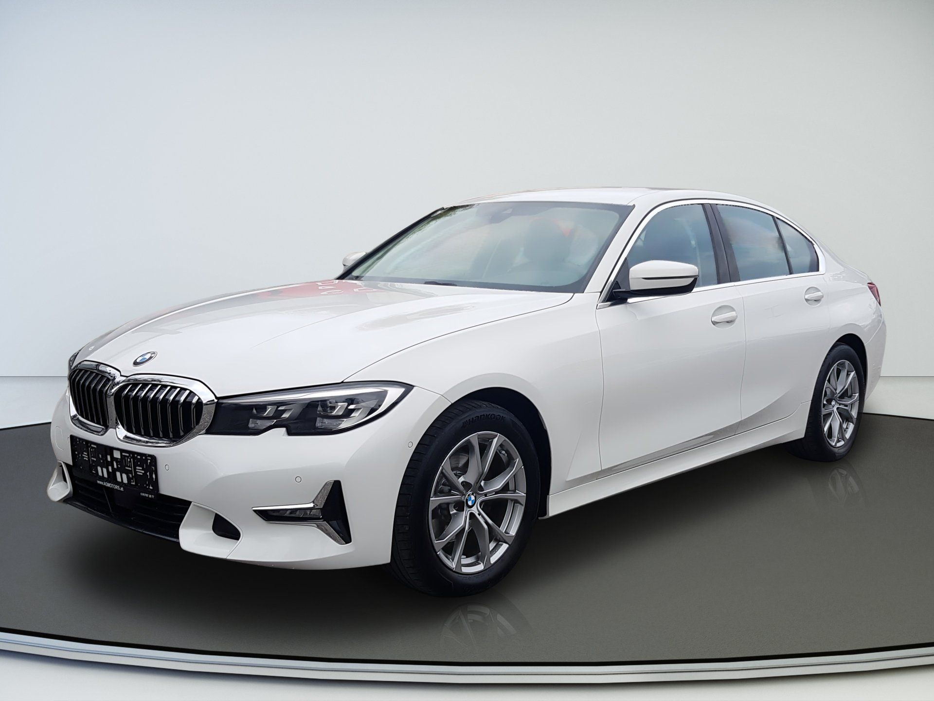 Biely sedan BMW na štúdiovom gramofóne, pohľad spredu z troch štvrtín na svetlosivom pozadí