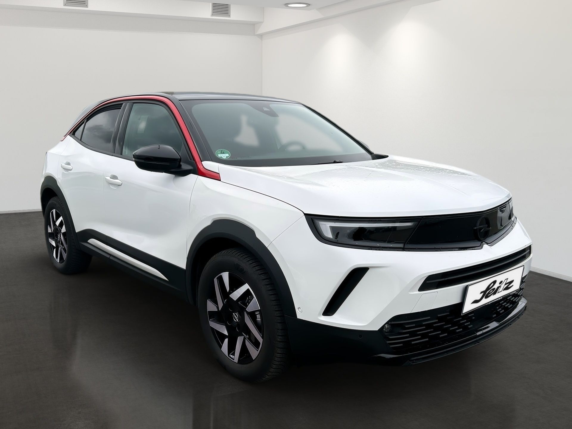 White compact SUV in a studio, shown from the front-left with black trim and red roof accents