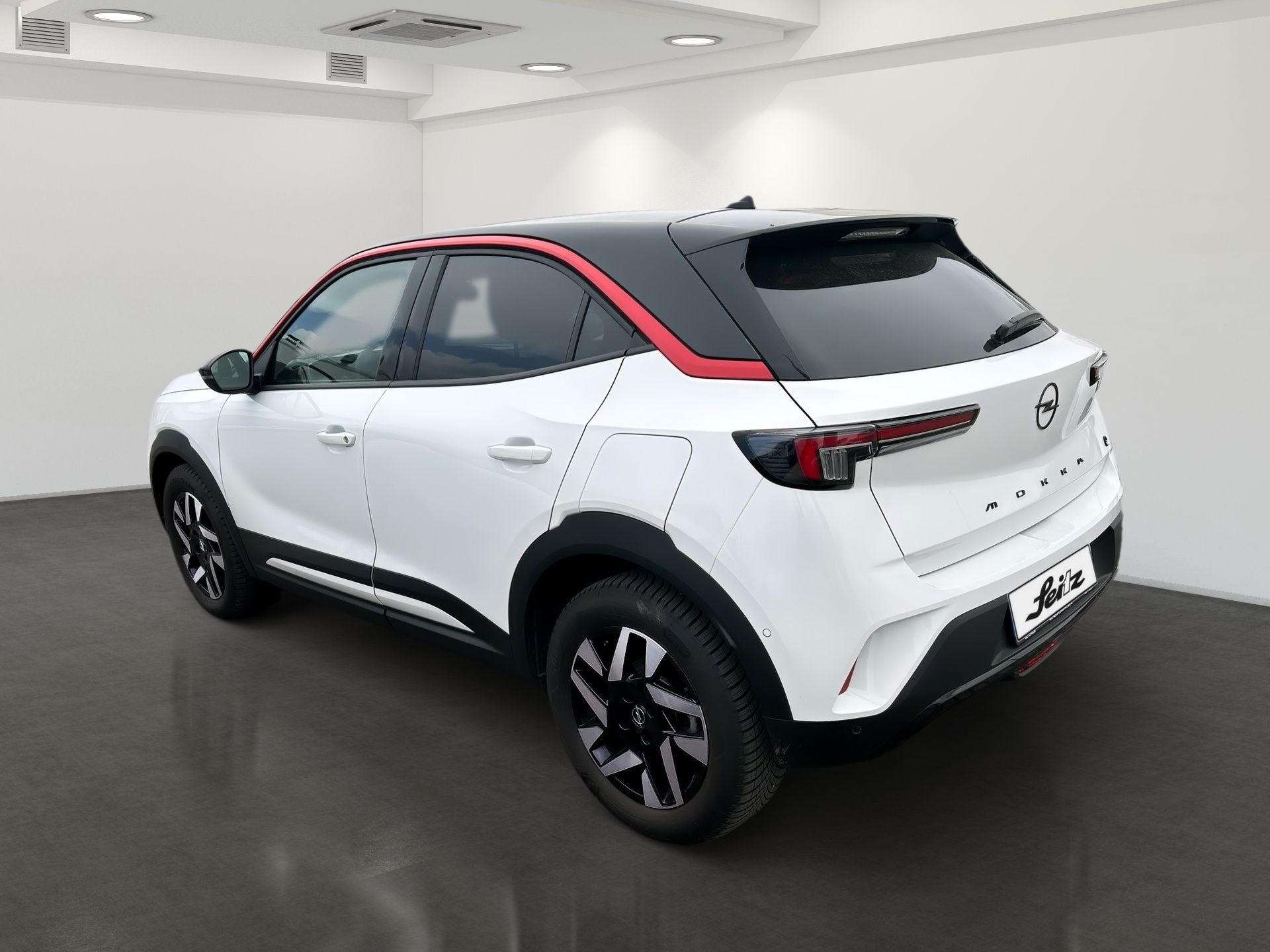 White compact SUV with black wheels and red roof accent, parked indoors in a showroom