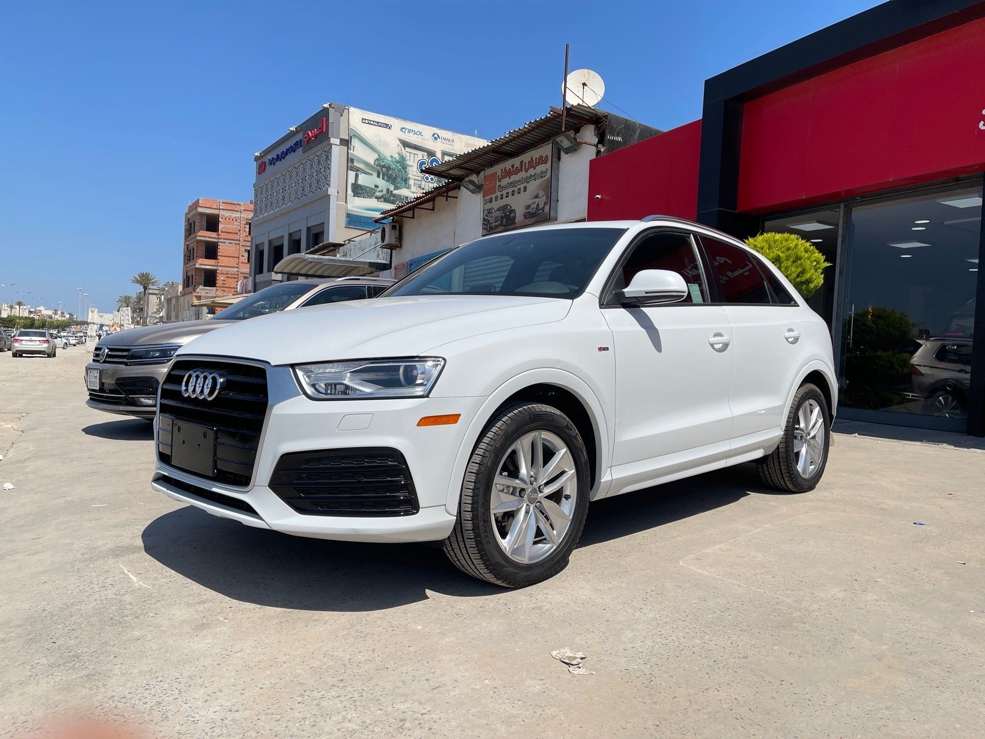 Biele SUV značky Audi zaparkované pred výkladom obchodu na slnečnej ulici.