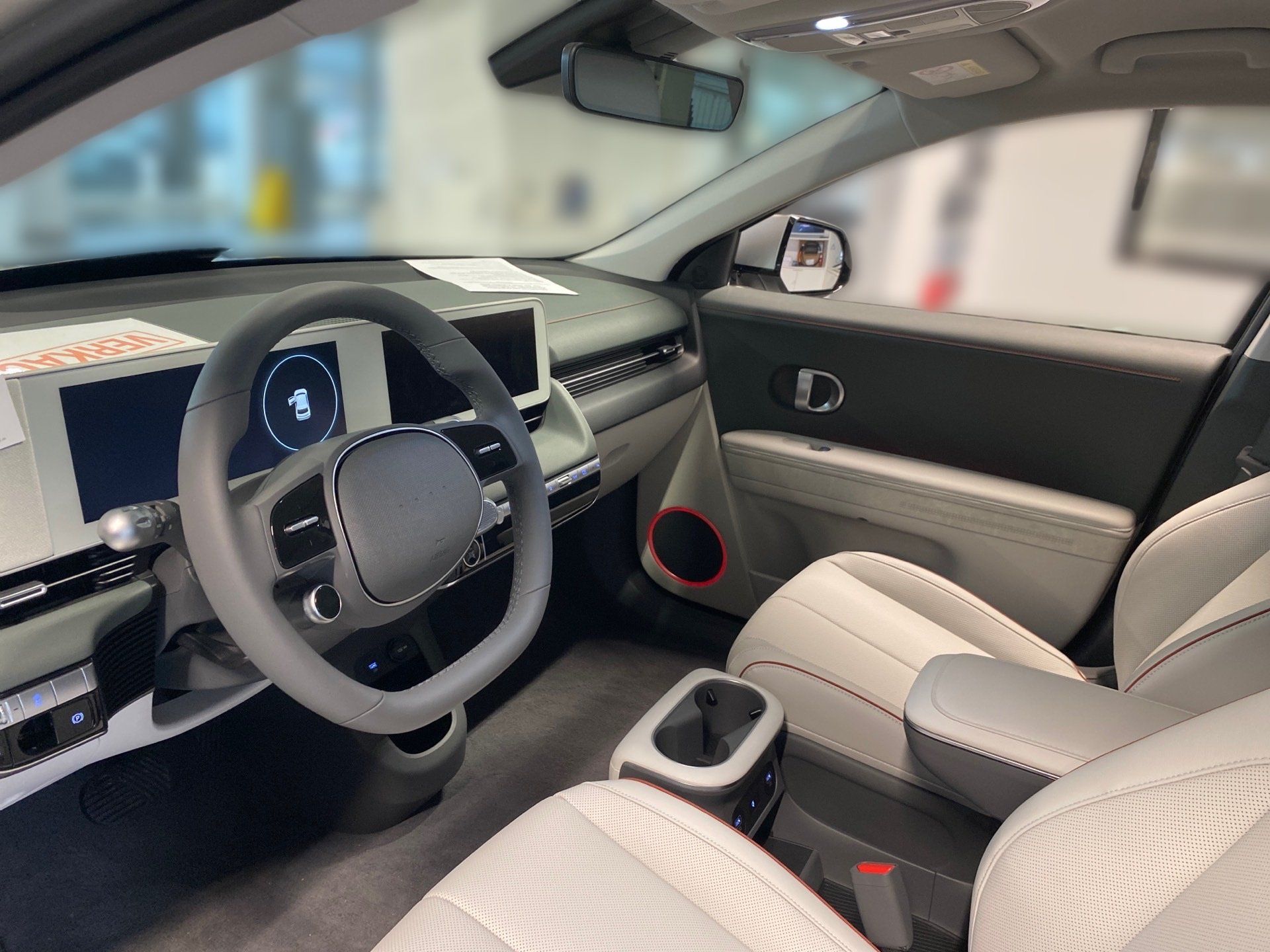 Modern car interior with light gray seats, steering wheel, dashboard, and red speaker accents