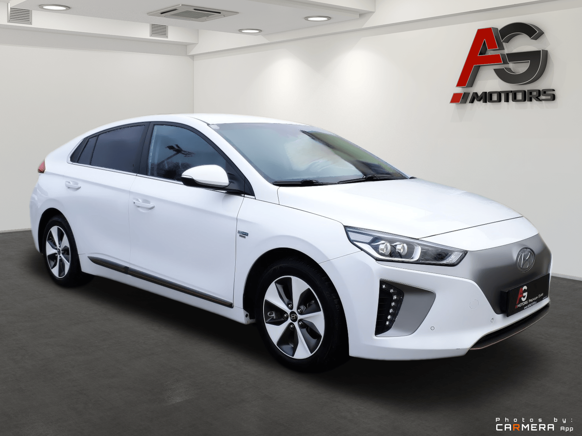 Biely sedan v showroome s nápisom AG Motors na stene