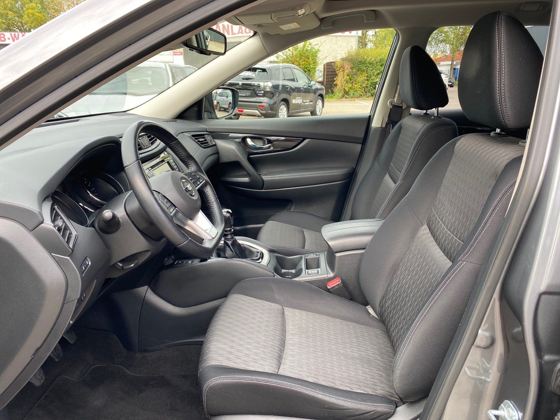 Car interior with gray cloth seats, steering wheel, and center console viewed from the open driver’s door
