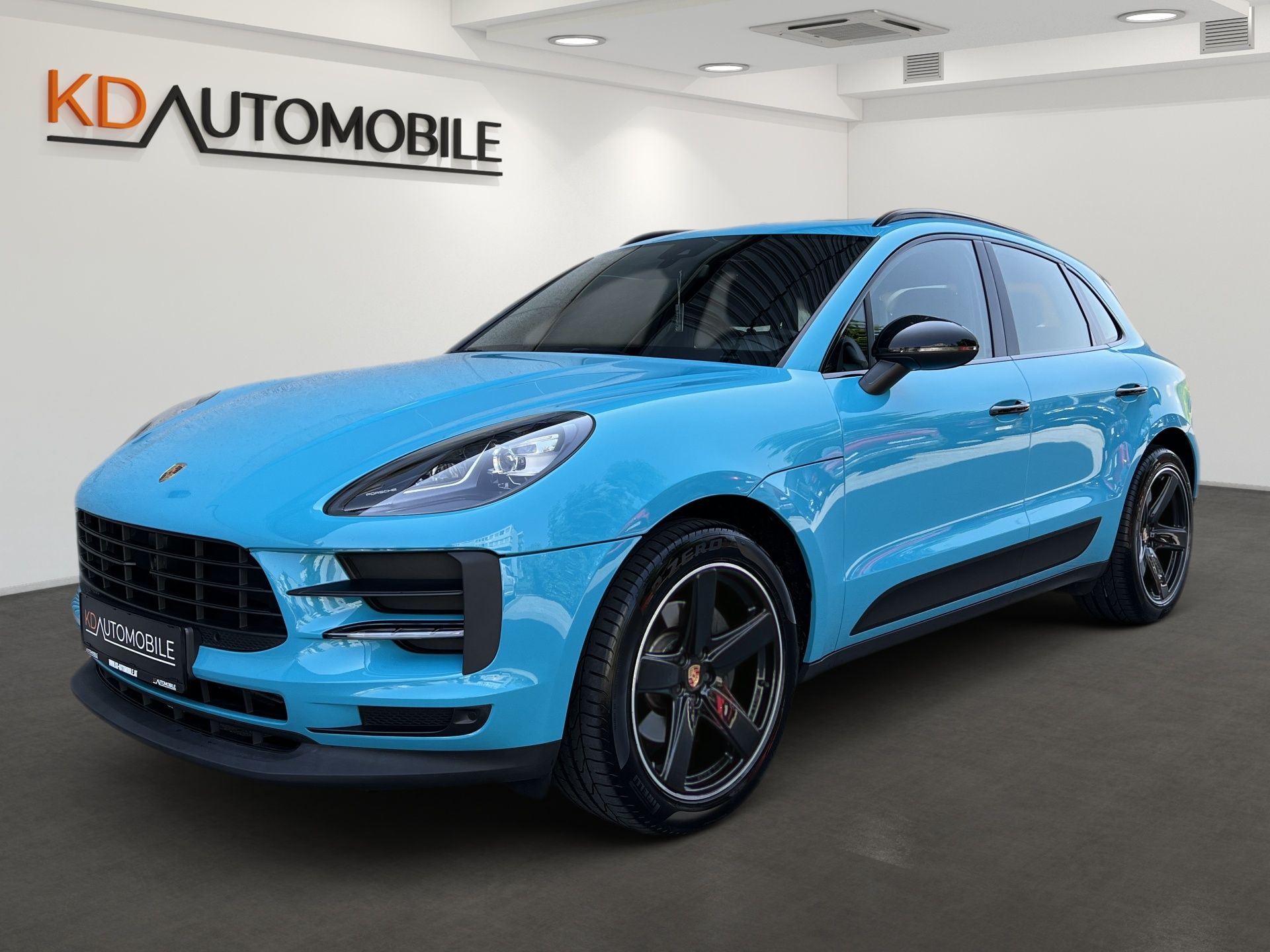 Blue Porsche SUV in a showroom with KDA Automobile branding on the wall