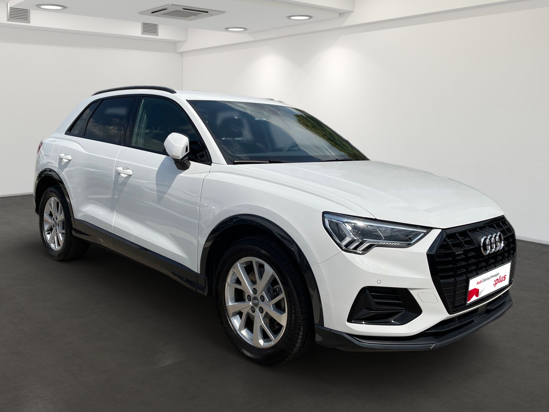 White Audi SUV parked indoors in a showroom, front-left view.