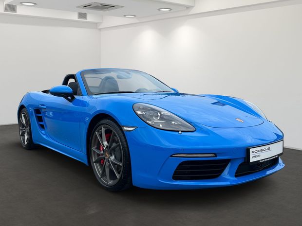 Ein blauer Porsche Boxster steht in einem digitalen Ausstellungsraum.