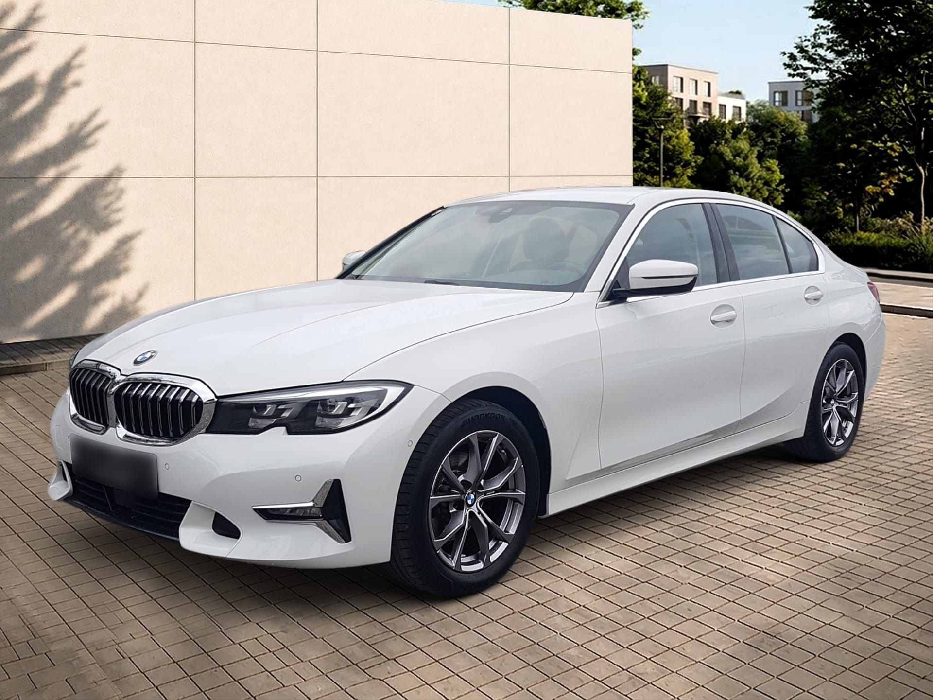 White BMW sedan parked on a brick driveway beside a beige wall outdoors
