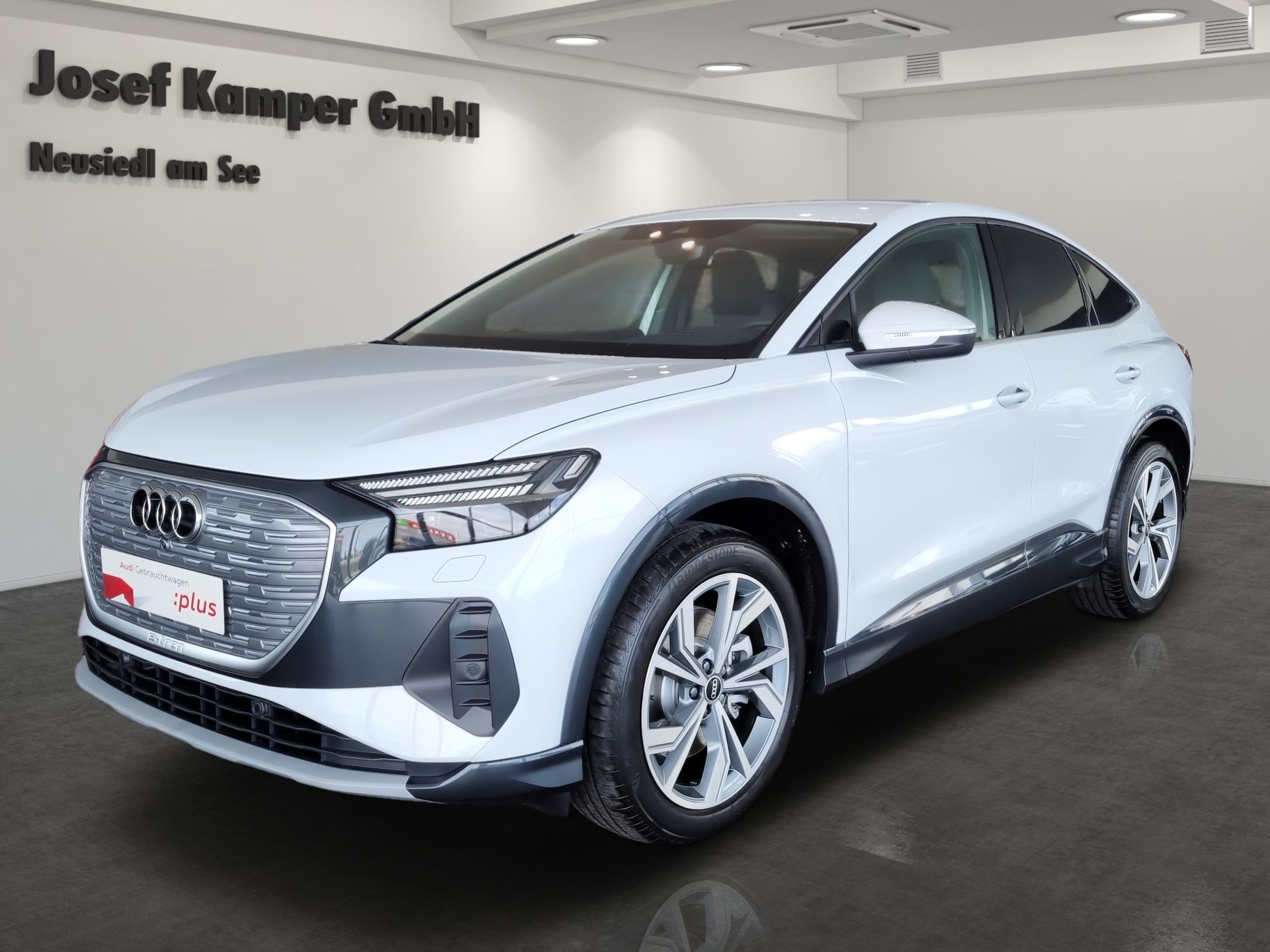White Audi electric SUV displayed in a showroom with a black floor and dealership signage on the wall