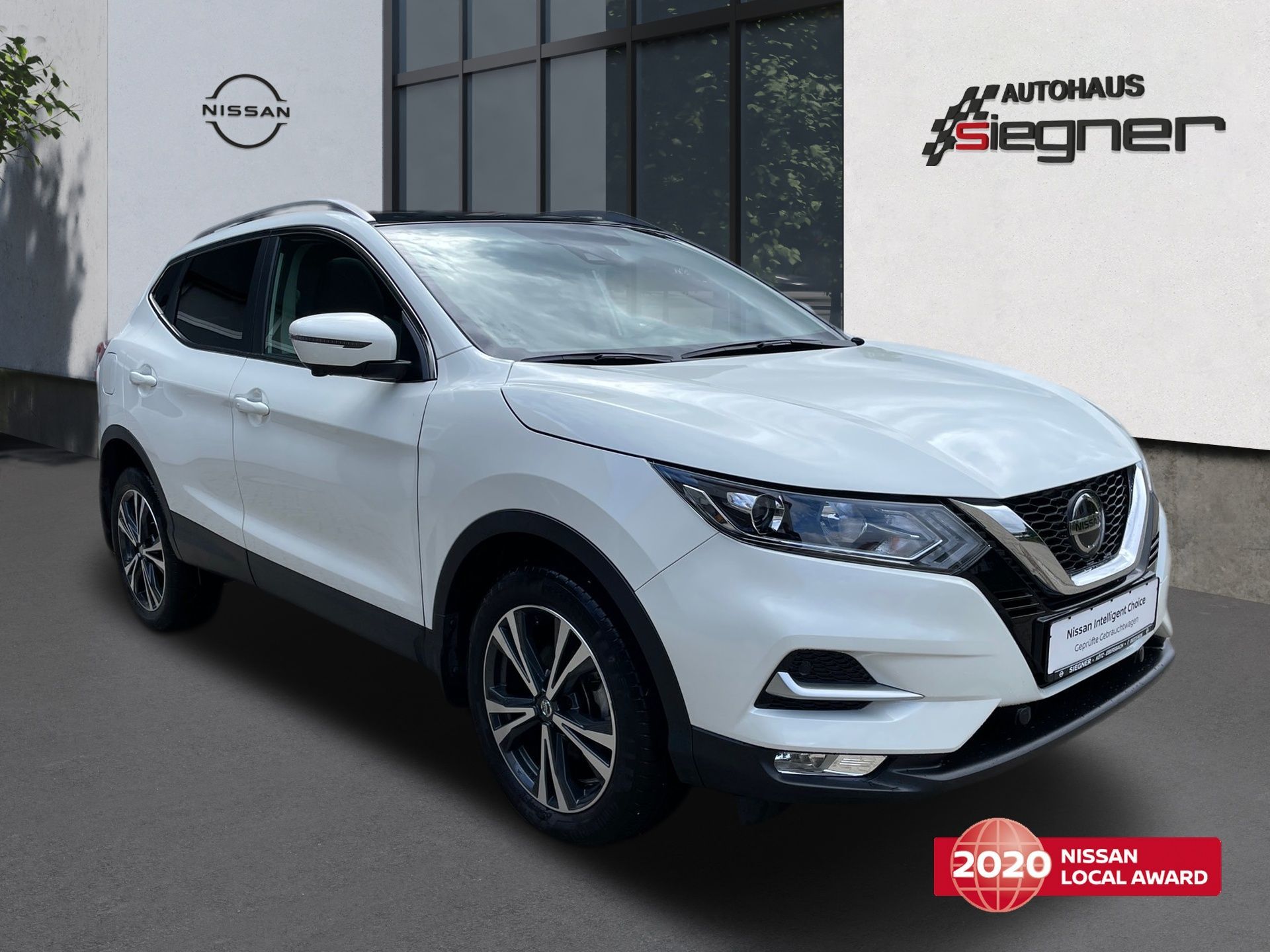 White Nissan SUV parked in a dealership showroom with Autohans Seigner branding on the wall