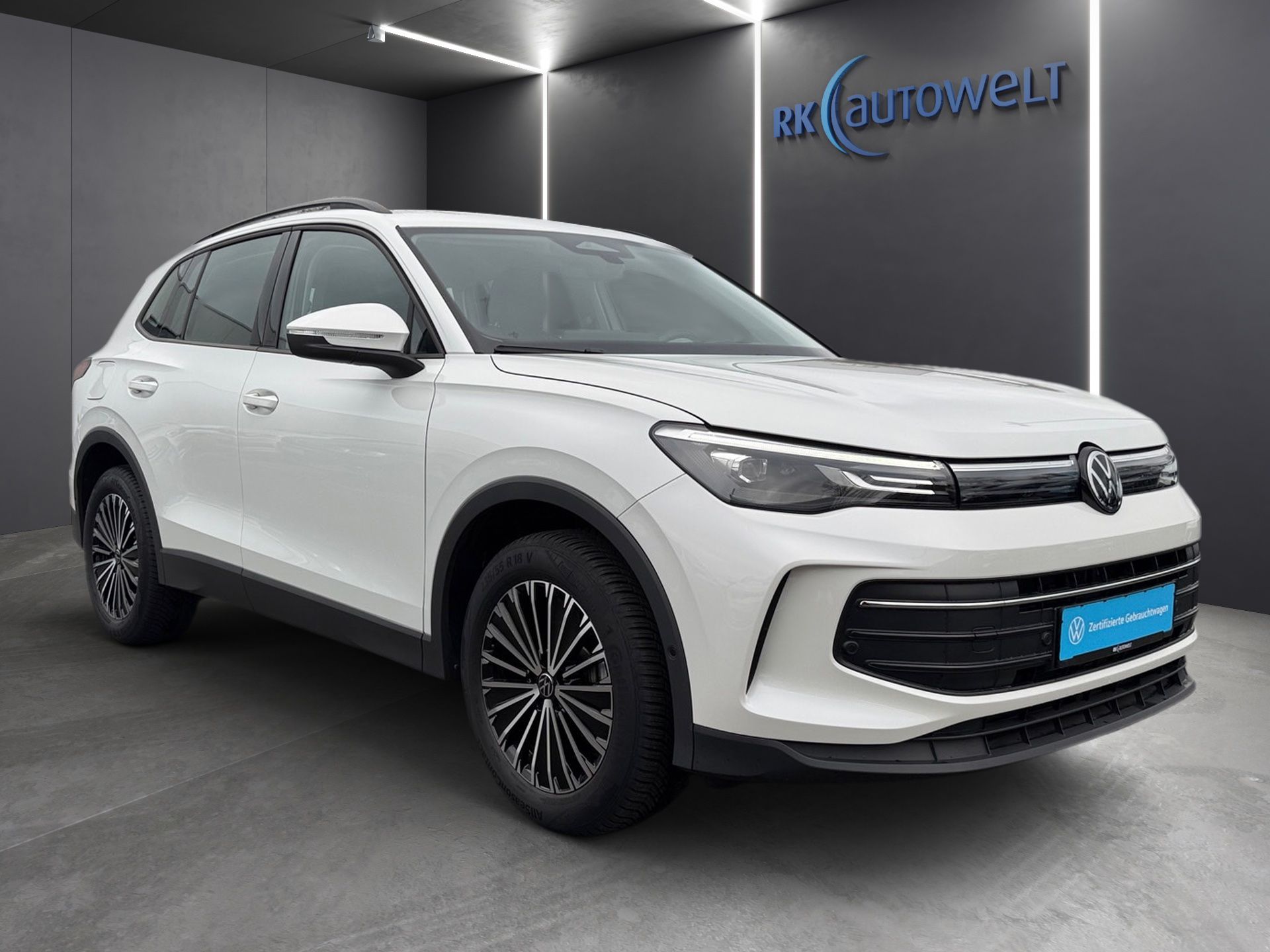 Weißer SUV im Ausstellungsraum, Dreiviertelansicht von vorn mit schwarzer Zierleiste und blauem Kennzeichen.