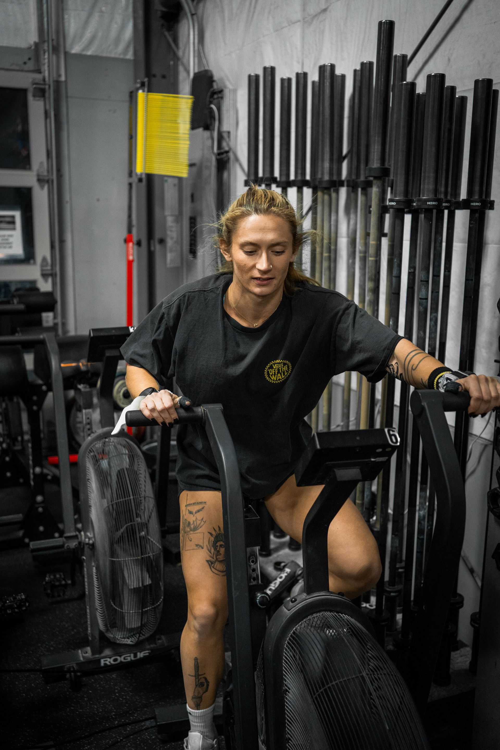 Woman on a stationary bike in a gym, gripping the handlebars and looking down.