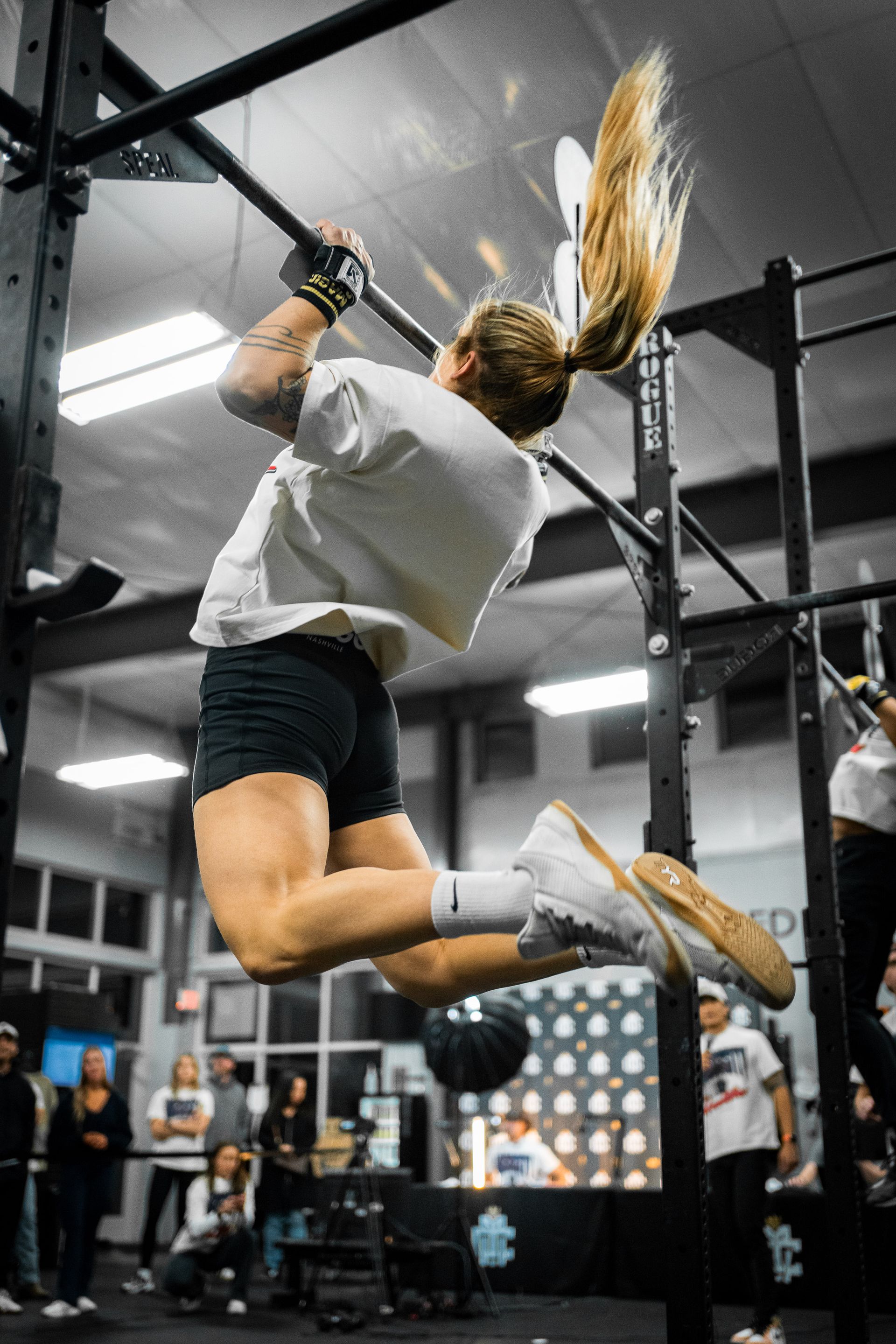 Athlete midair doing a pull-up on gym rings, black-and-white gym setting