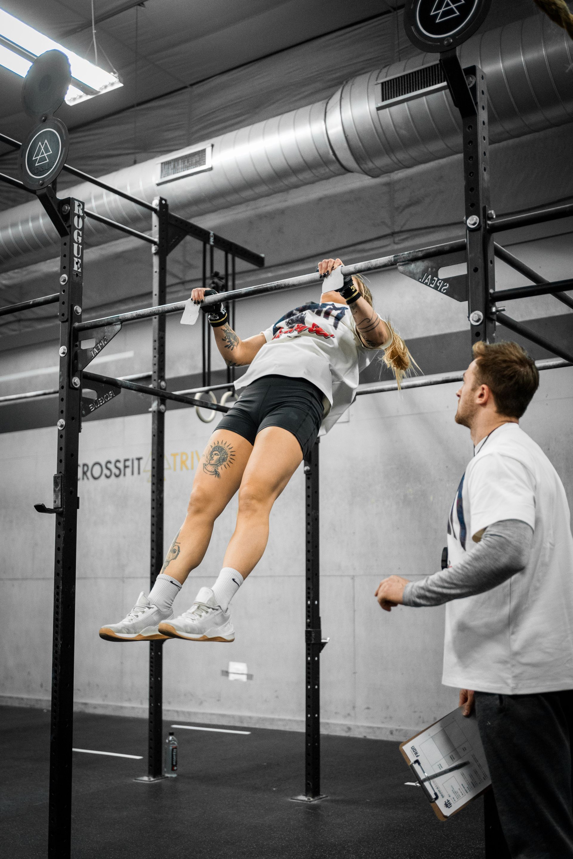 Athlete doing pull-up on gym rig while a coach watches nearby
