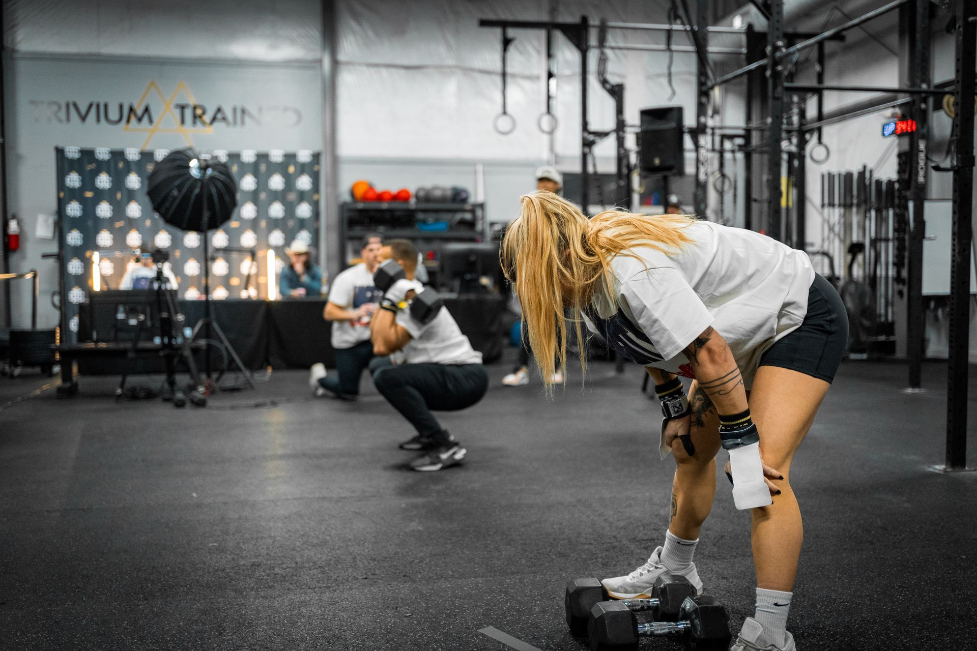 People exercising with dumbbells in a gym, one bending forward in the foreground