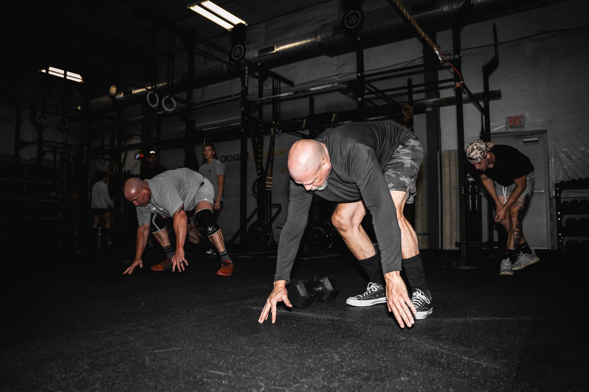 People stretching on a gym floor in a dark fitness studio, preparing for exercise.
