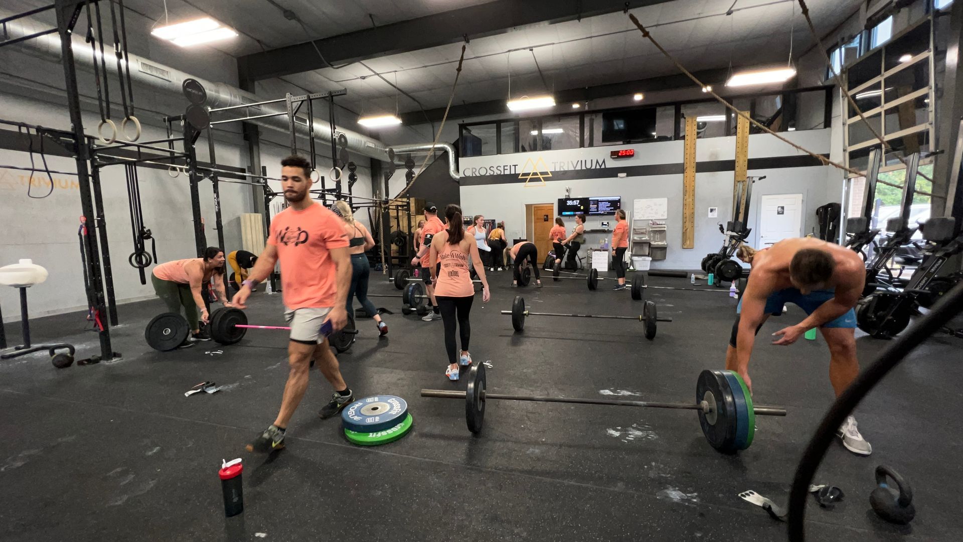 People exercising in a gym with barbells and plates on the floor.