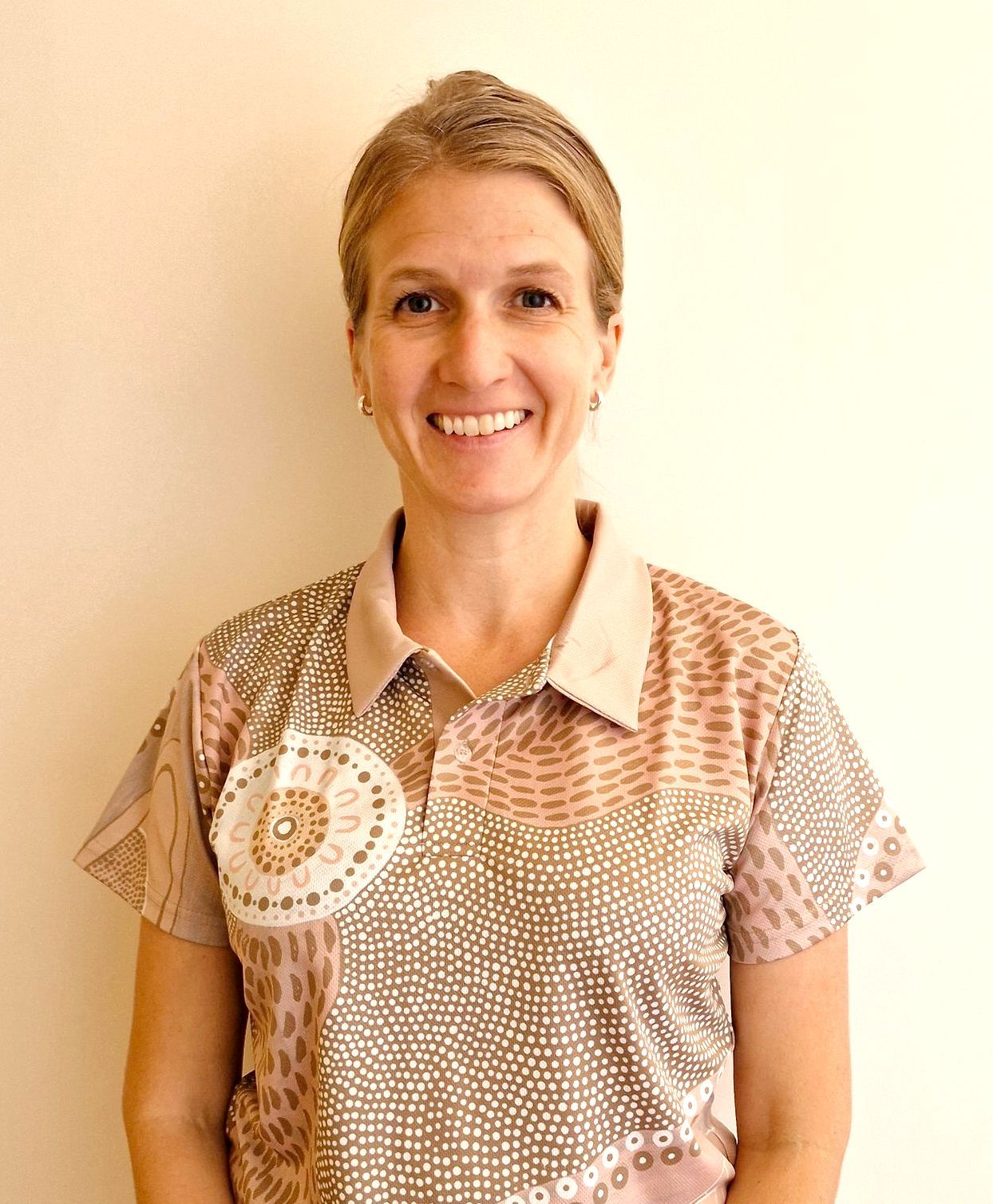 Smiling person in a patterned beige shirt against a plain light background
