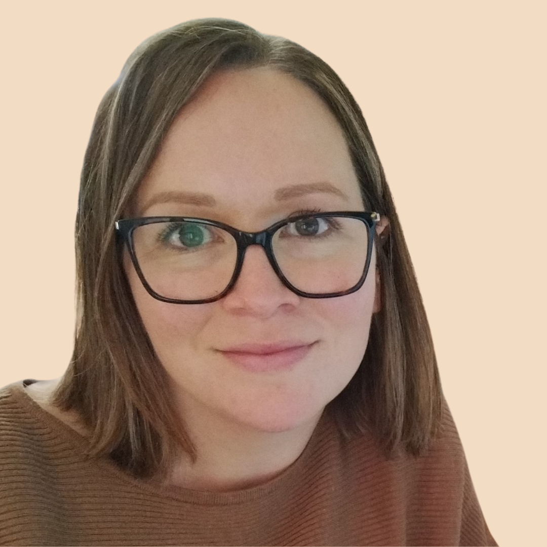 Smiling person with glasses and shoulder-length hair in a brown sweater against a beige background