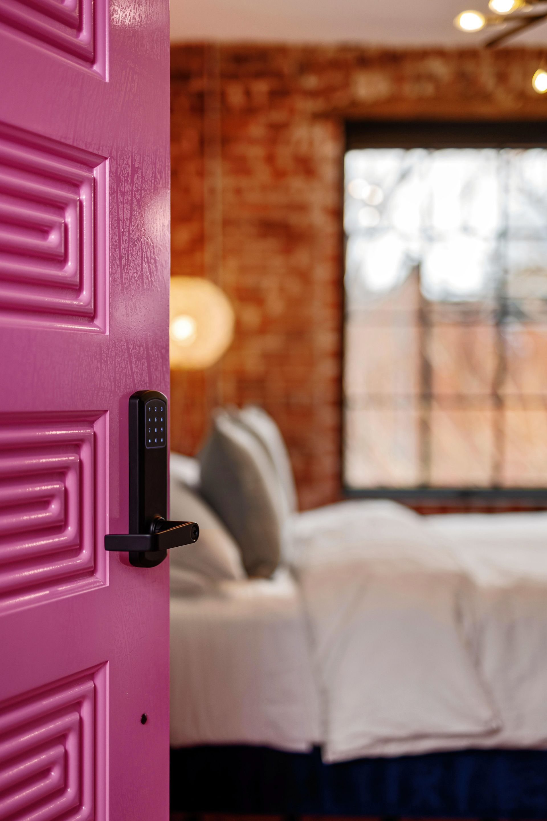 Open pink door to a cozy bedroom with brick walls and a large window.