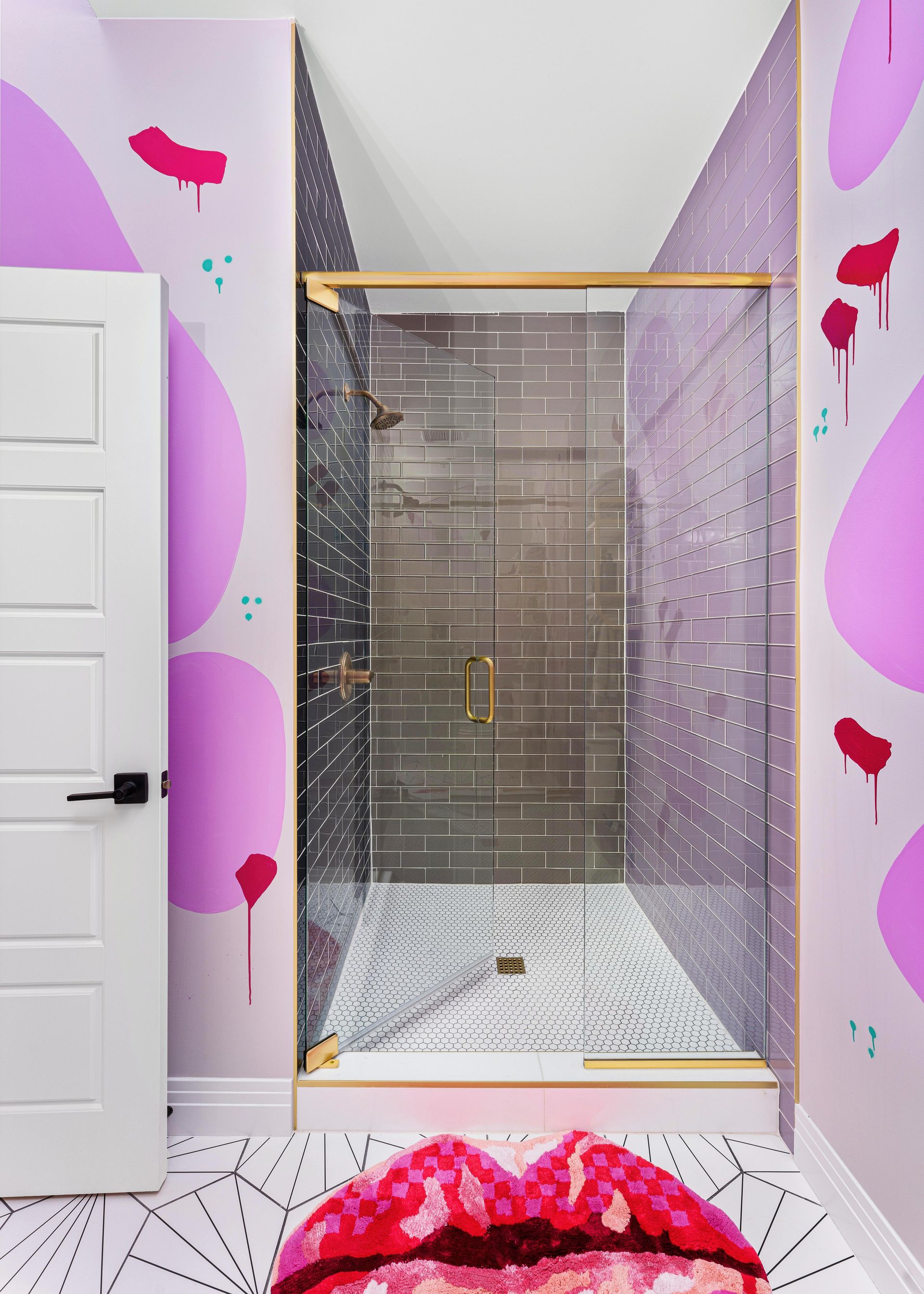 Pink-themed bathroom with a glass shower stall and white door, seen through a narrow doorway