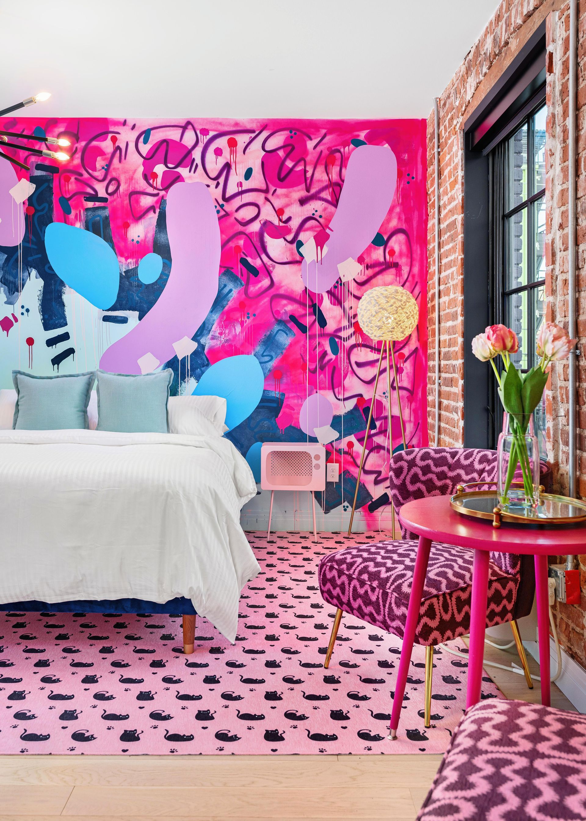 Bright pink graffiti-style bedroom with white bed, floral decor, and a windowed wall of glass doors