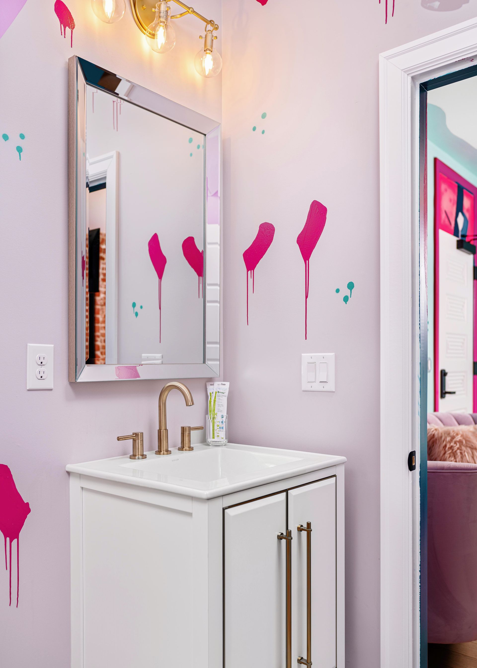 Pink-themed bathroom vanity with gold fixtures and a mirror, accented by pink wall decor and string lights