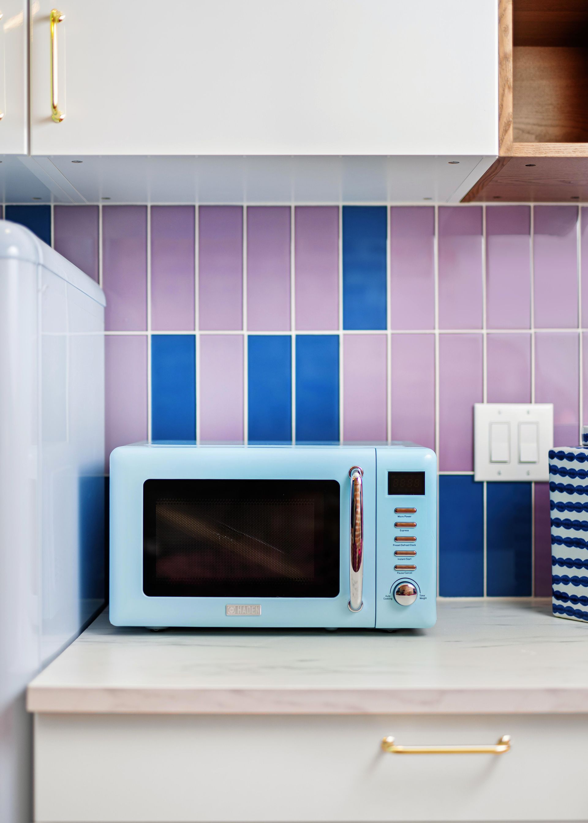 Light blue microwave on a white kitchen counter with pink and blue tiled backsplash