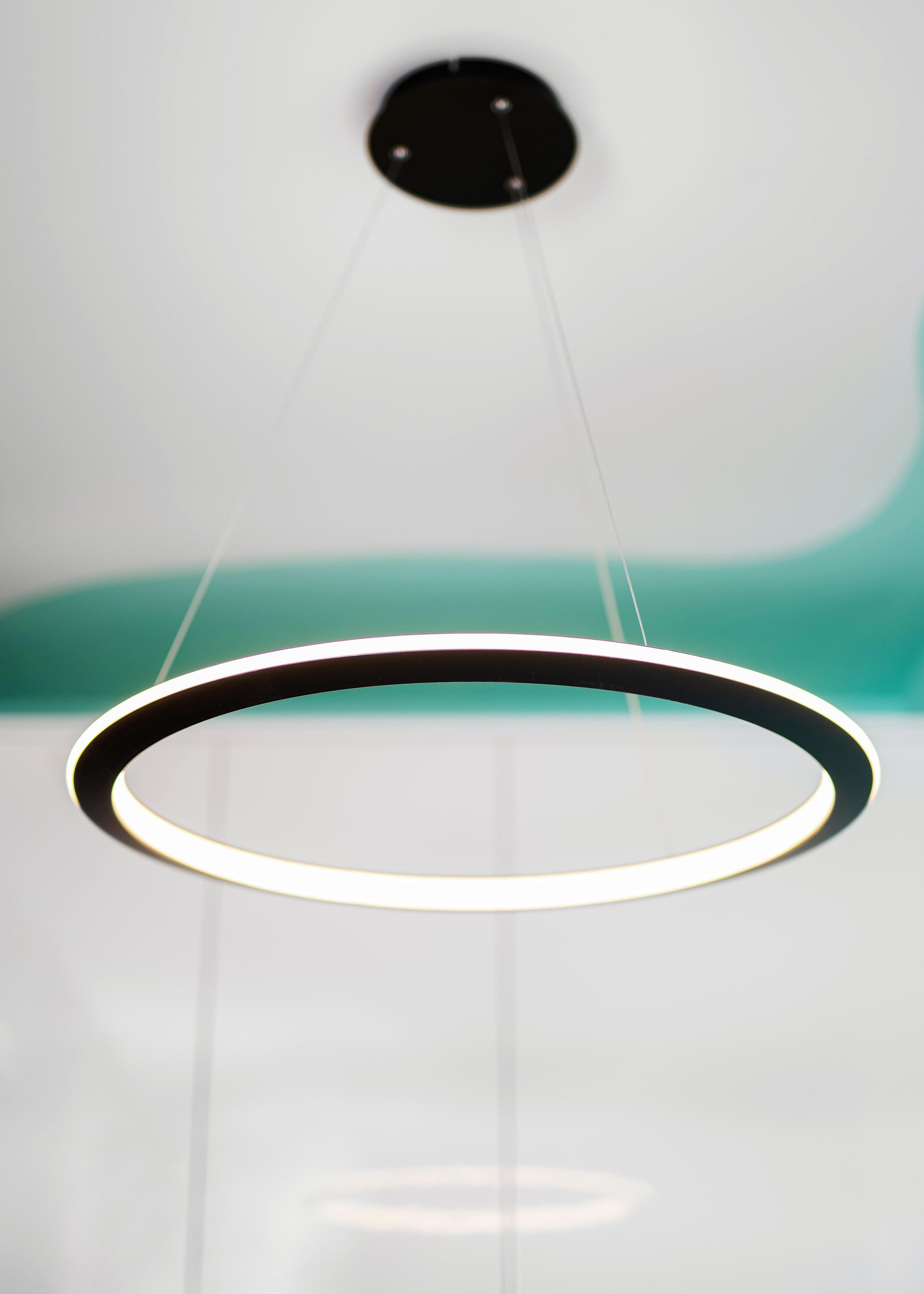 Modern circular pendant light with black rim and glowing white center, hanging from the ceiling