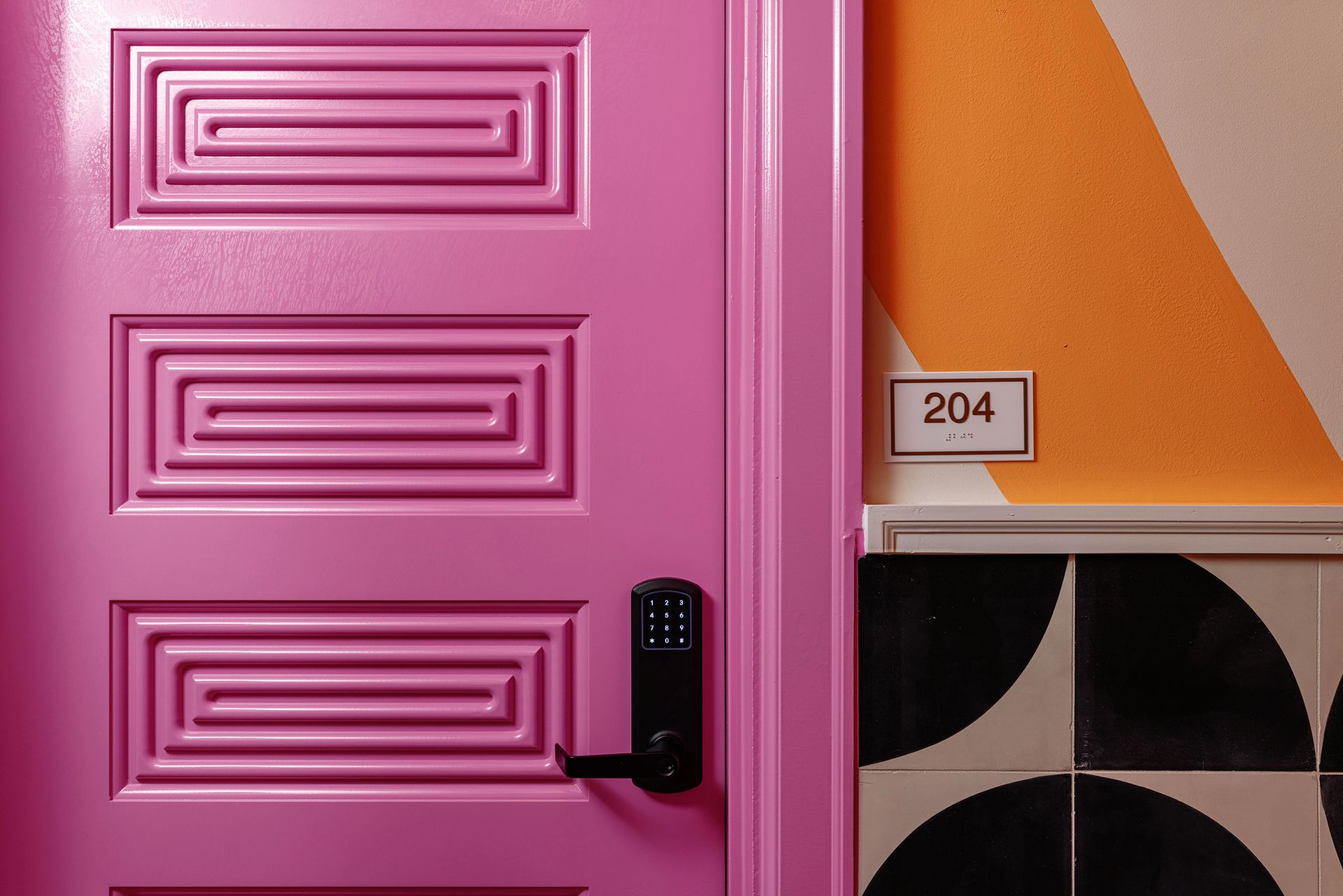 Pink door with black handle beside orange-and-white wall and room number 204