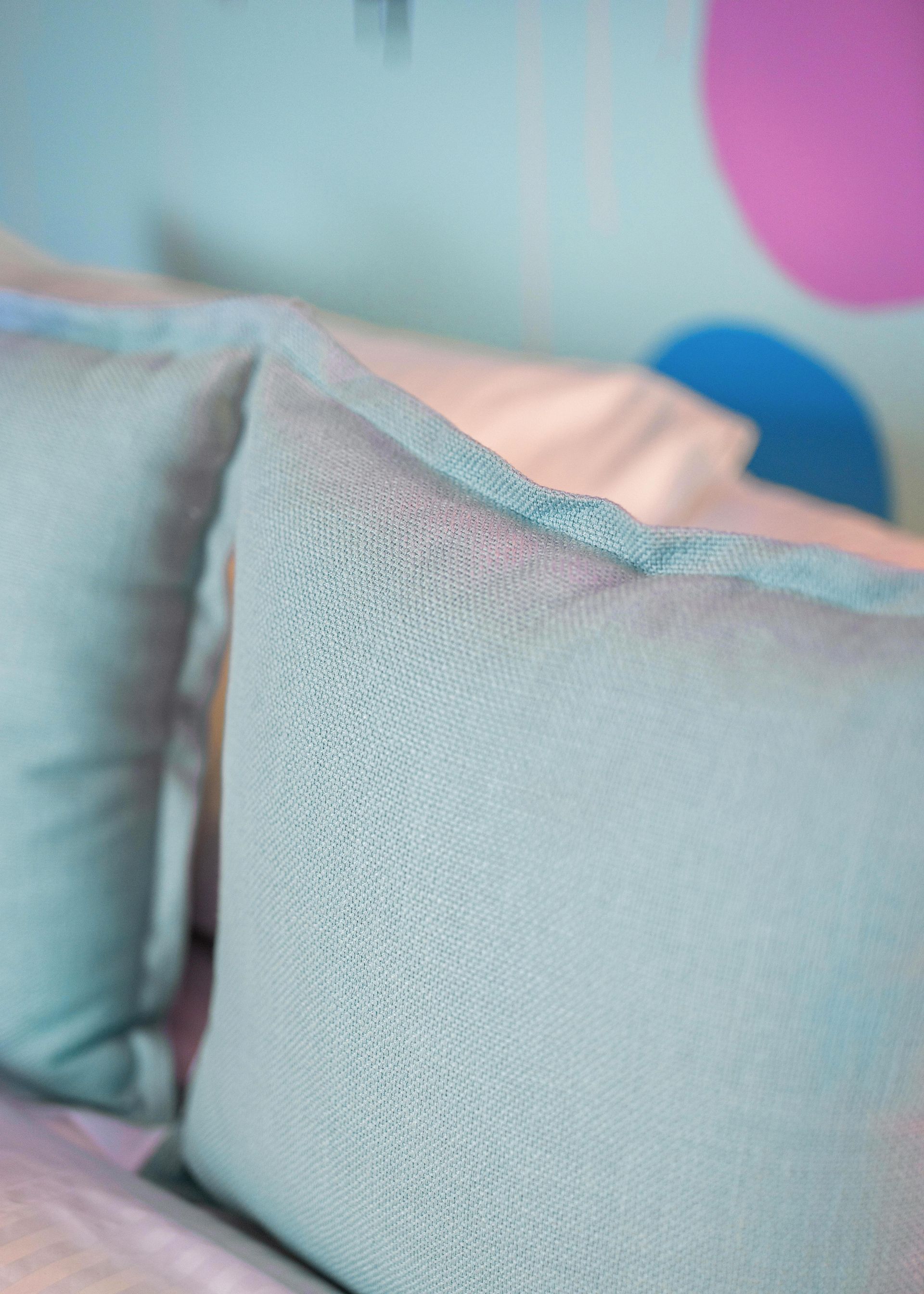 Light blue pillows on a bed with a pastel pink and blue background