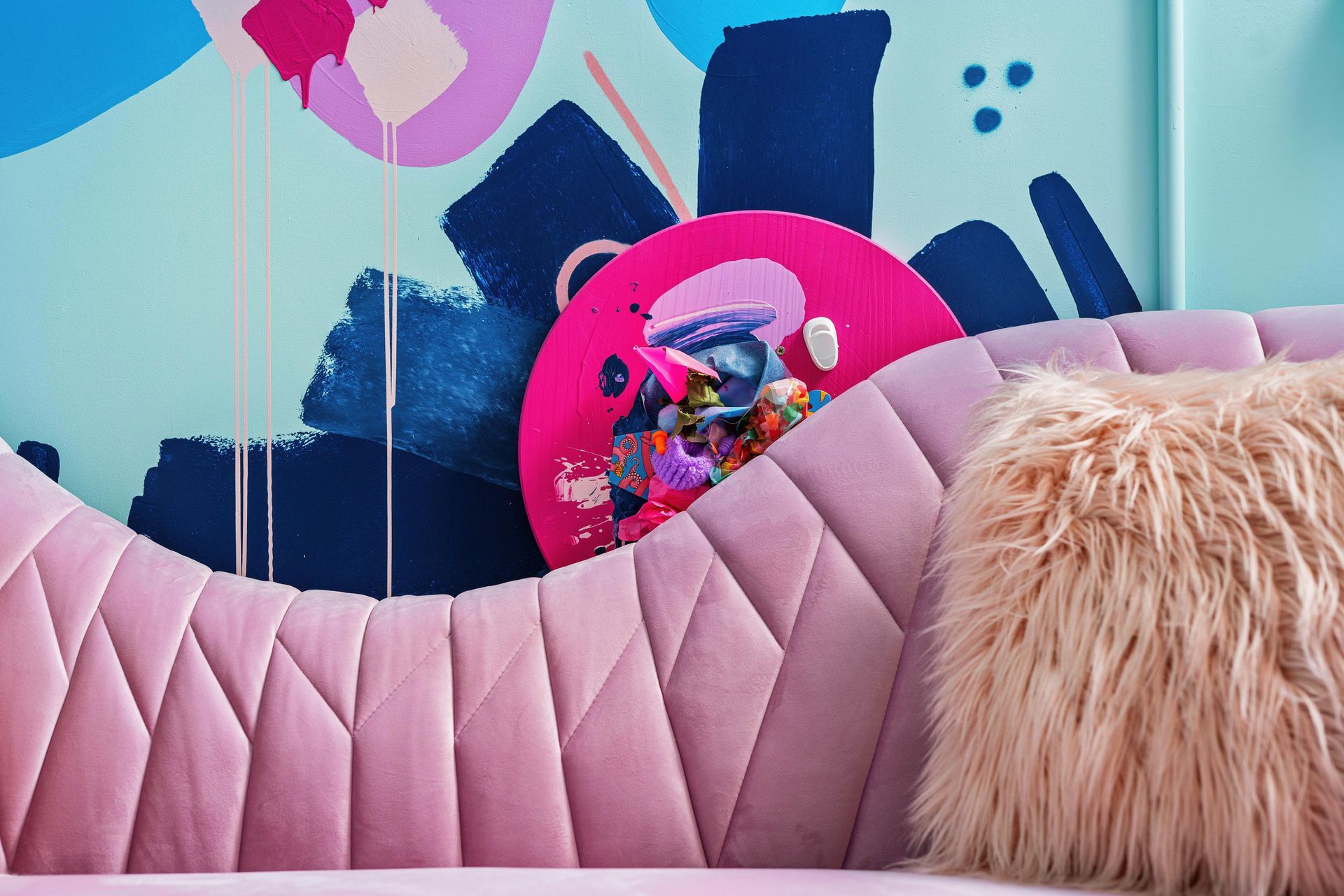 Pink tufted sofa with fluffy pillow in front of colorful wall art and a bright pink circular decor piece