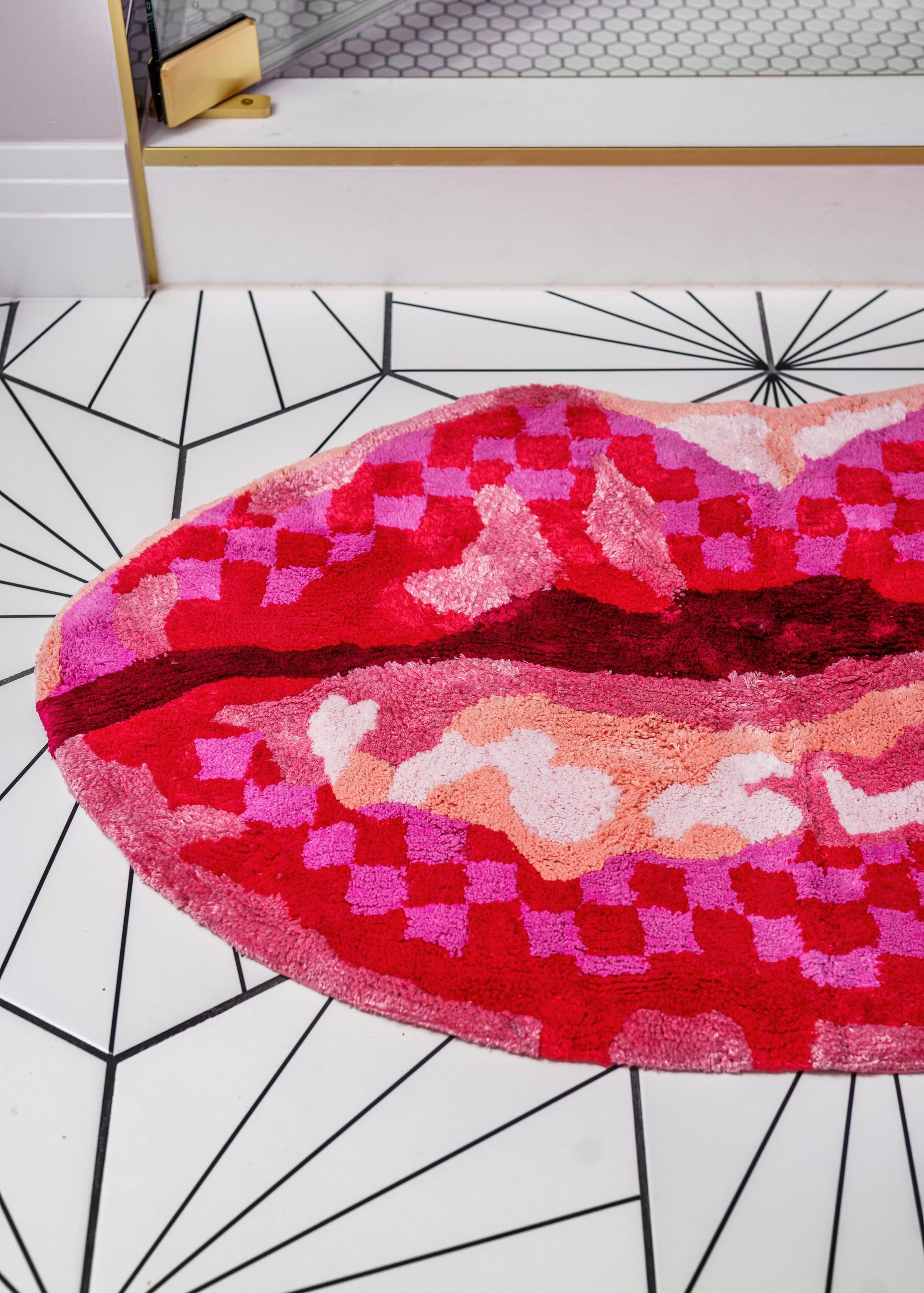 Close-up of a pink heart-shaped rug on a white geometric floor, with a bed in the background