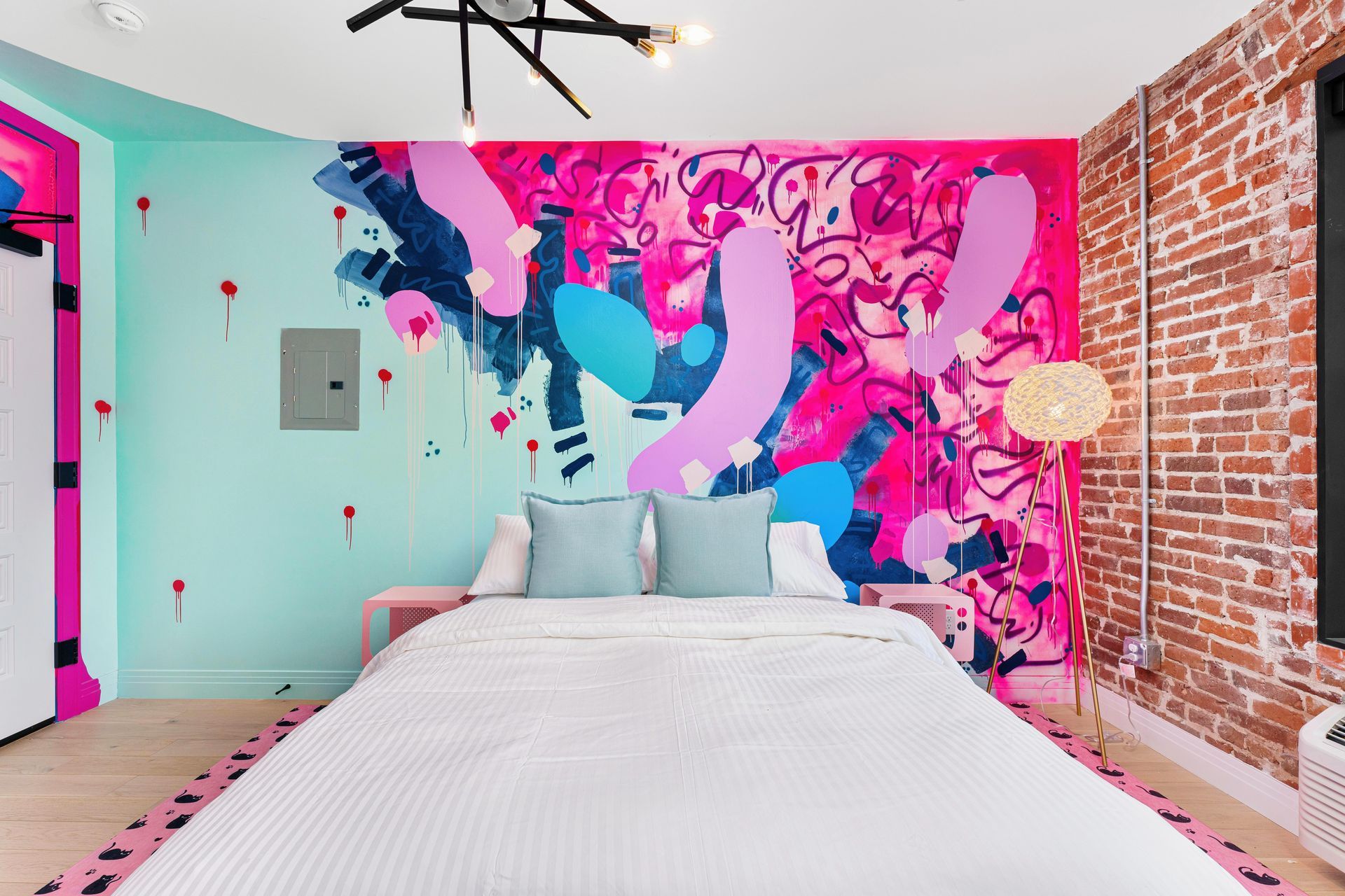 Colorful bedroom with pink mural wall, turquoise accent wall, brick side wall, and white bed