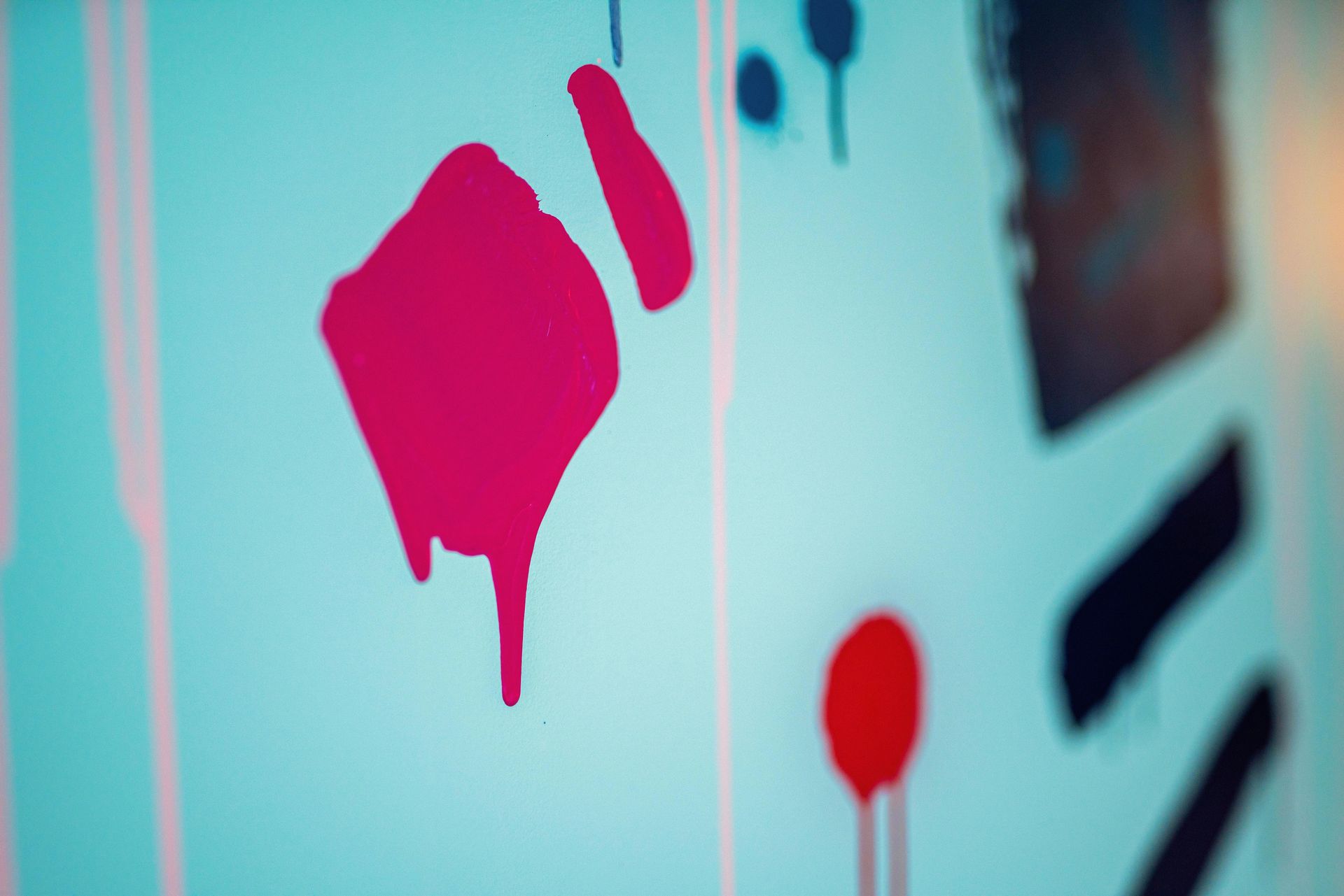 Abstract pink paint drips on a light blue wall with blurred dark shapes in the background