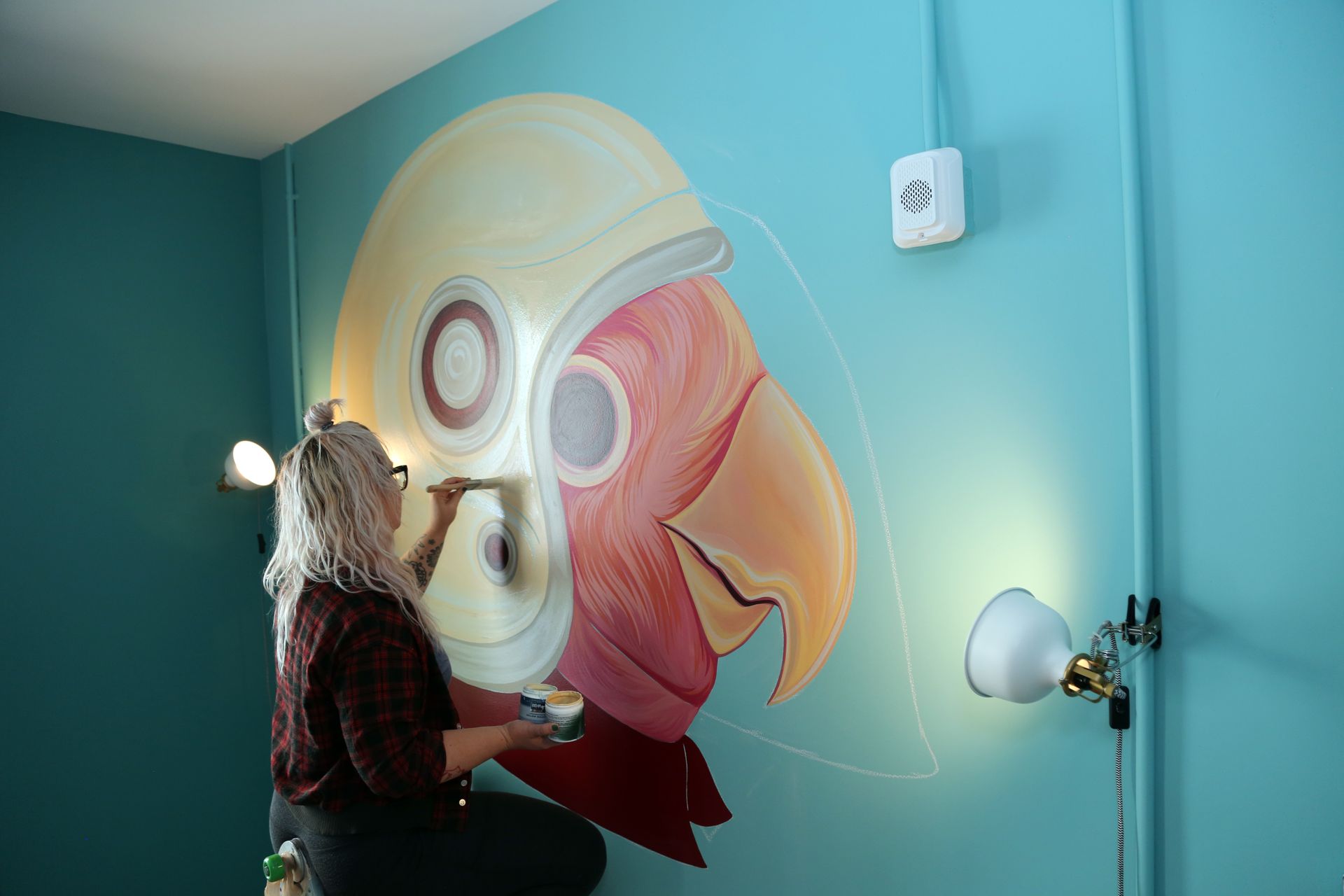 Person painting a large colorful abstract mural on a teal wall in a room