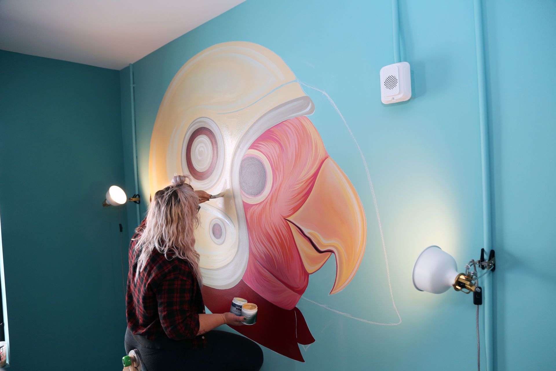 Person painting a colorful mural on a teal wall in a room